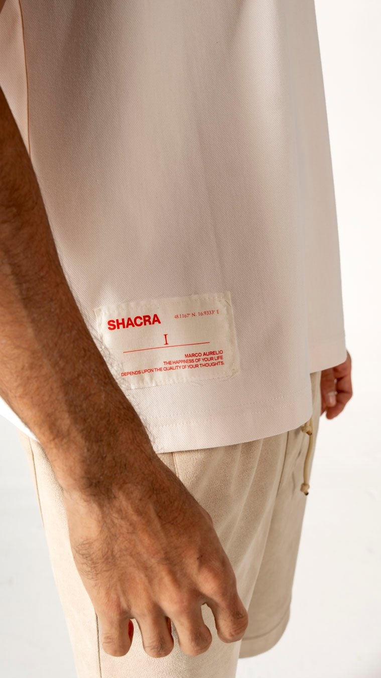 Shacra clothing brand label on beige shirt, close-up of fashion label with red text, modern streetwear design, minimalistic style, high-quality fabric, authentic casual apparel, trendy fashion statement, black male model, contemporary urban fashion, stylish men’s clothing, contemporary fashion accessories, latest apparel trends.