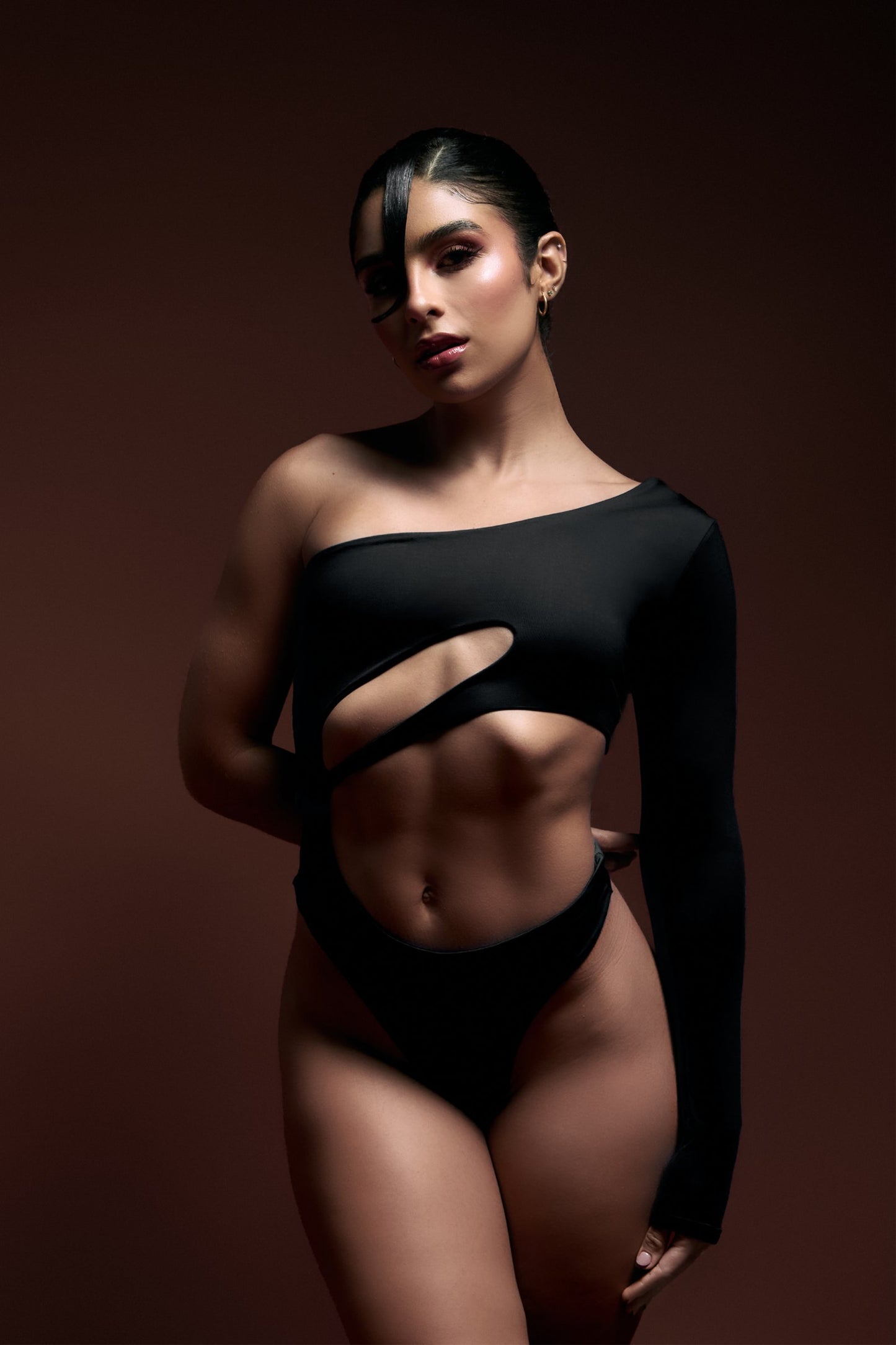 Striking woman wearing a black cut-out fashion top with an asymmetrical design, showcasing modern, high-end fashion and body confidence.