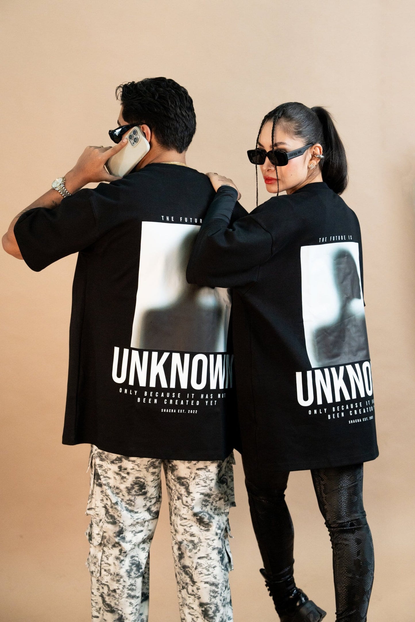Modern streetwear fashion featuring stylish adults in matching "UNKNOWN" graphic t-shirts,paired with trendy accessories like sunglasses and statement jewelry, showcasing contemporary urban style.