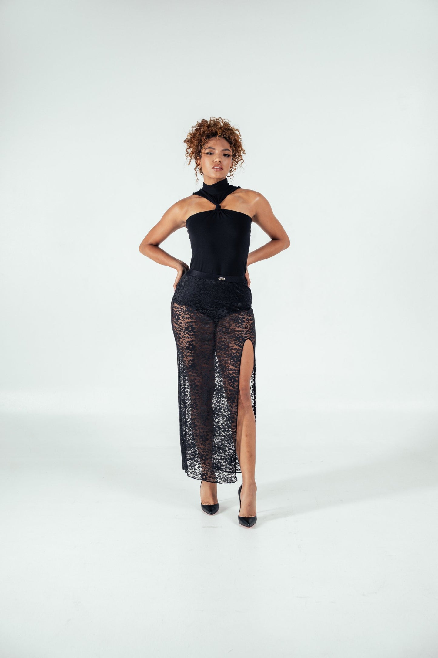 Elegant woman modeling stylish black lace high-slit skirt and sleeveless top in a minimalist studio setting, showcasing fashion and style from Shacra.