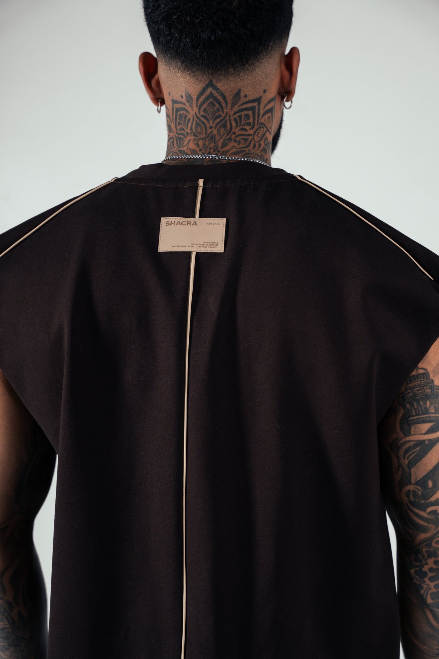 High-fashion streetwear model showcasing a black sleeveless top with beige piping, featuring a SHACRA tag on the back, highlighting modern urban clothing and stylish apparel from Shacra.