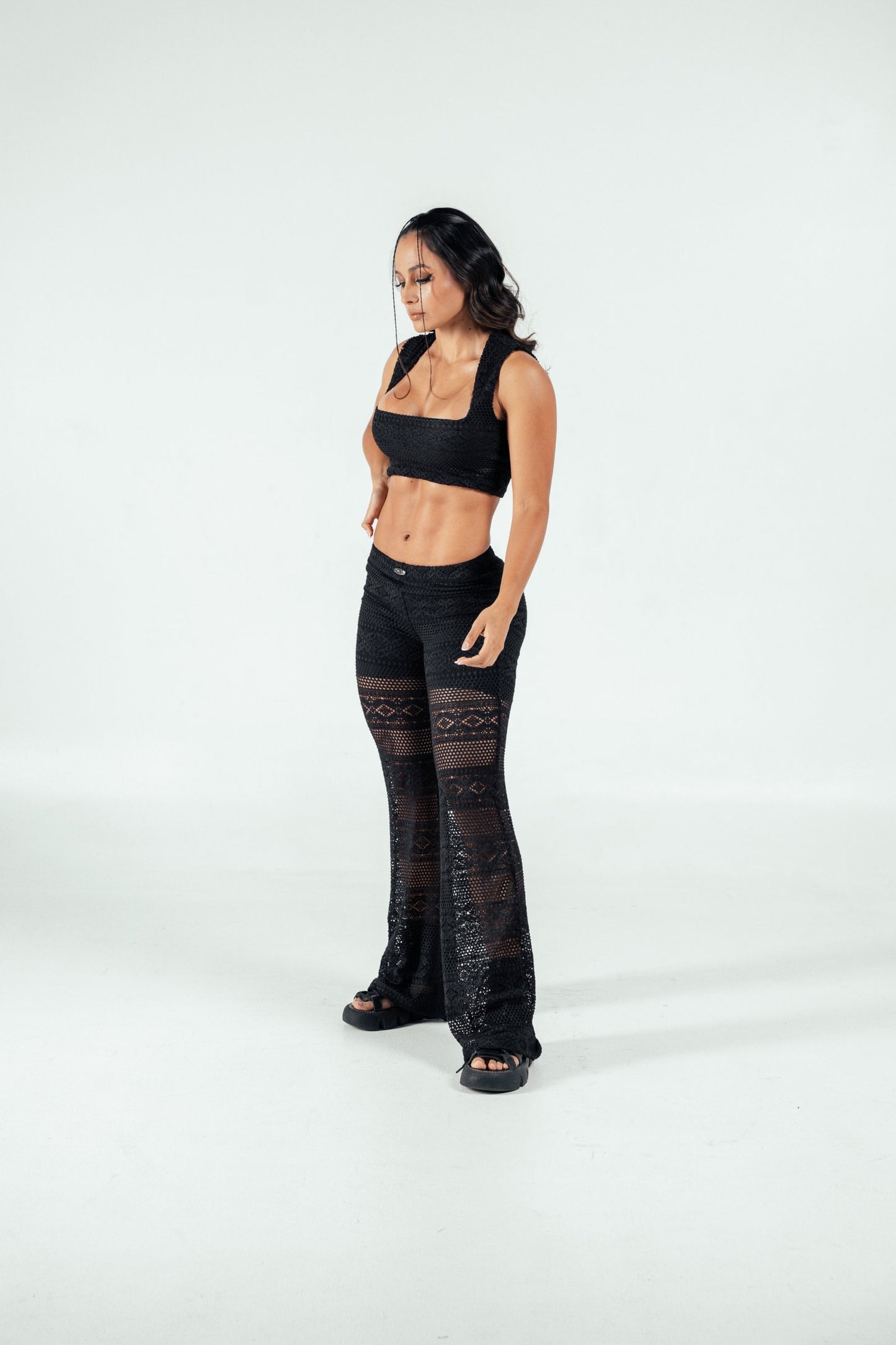 Stylish woman wearing black crochet crop top and wide-leg crochet pants, fashion-forward swimwear or resort outfit, on white background.