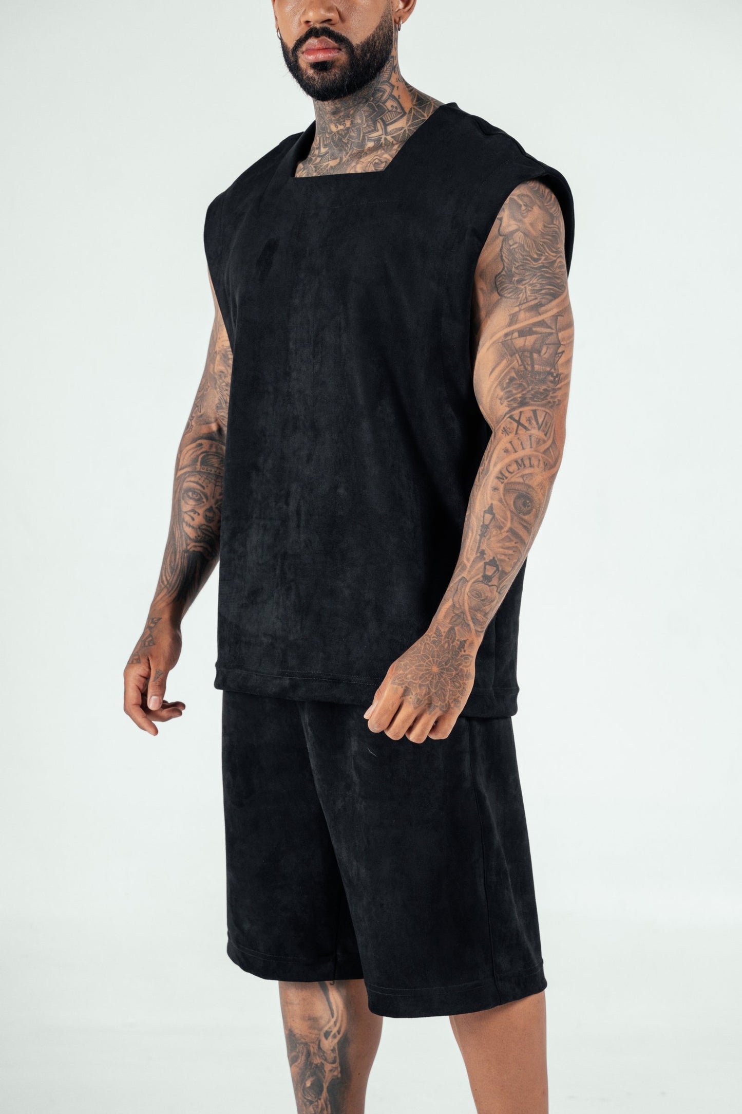 Bold photo of a tattooed male model wearing a black sleeveless top and matching shorts, showcasing contemporary streetwear fashion from Shacra, emphasizing quality and stylish casual clothing.