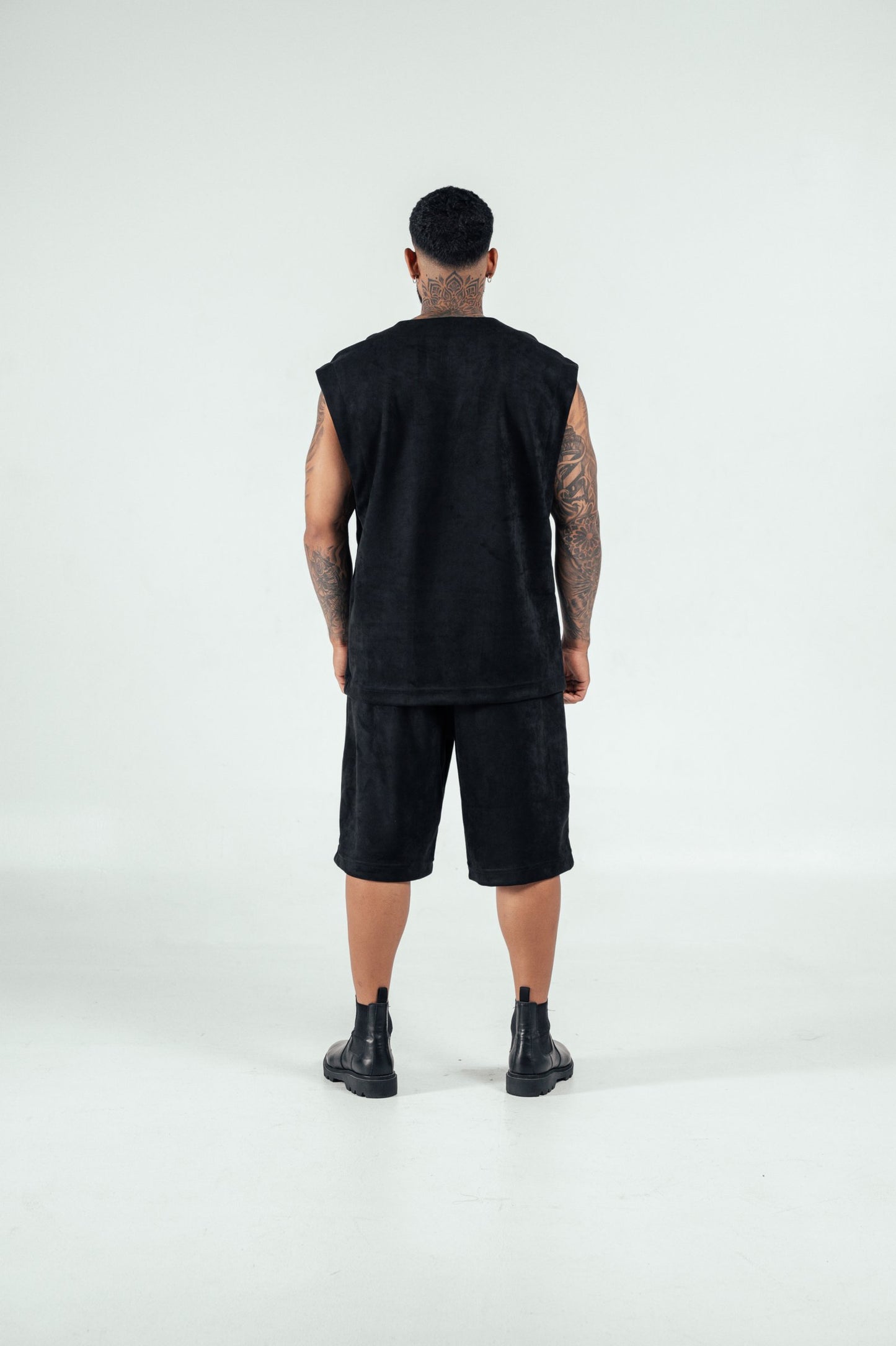 Modern streetwear fashion look featuring a man in all-black outfit with sleeveless top, shorts, and combat boots, showcasing edgy style and tattoos for urban fashion inspiration.