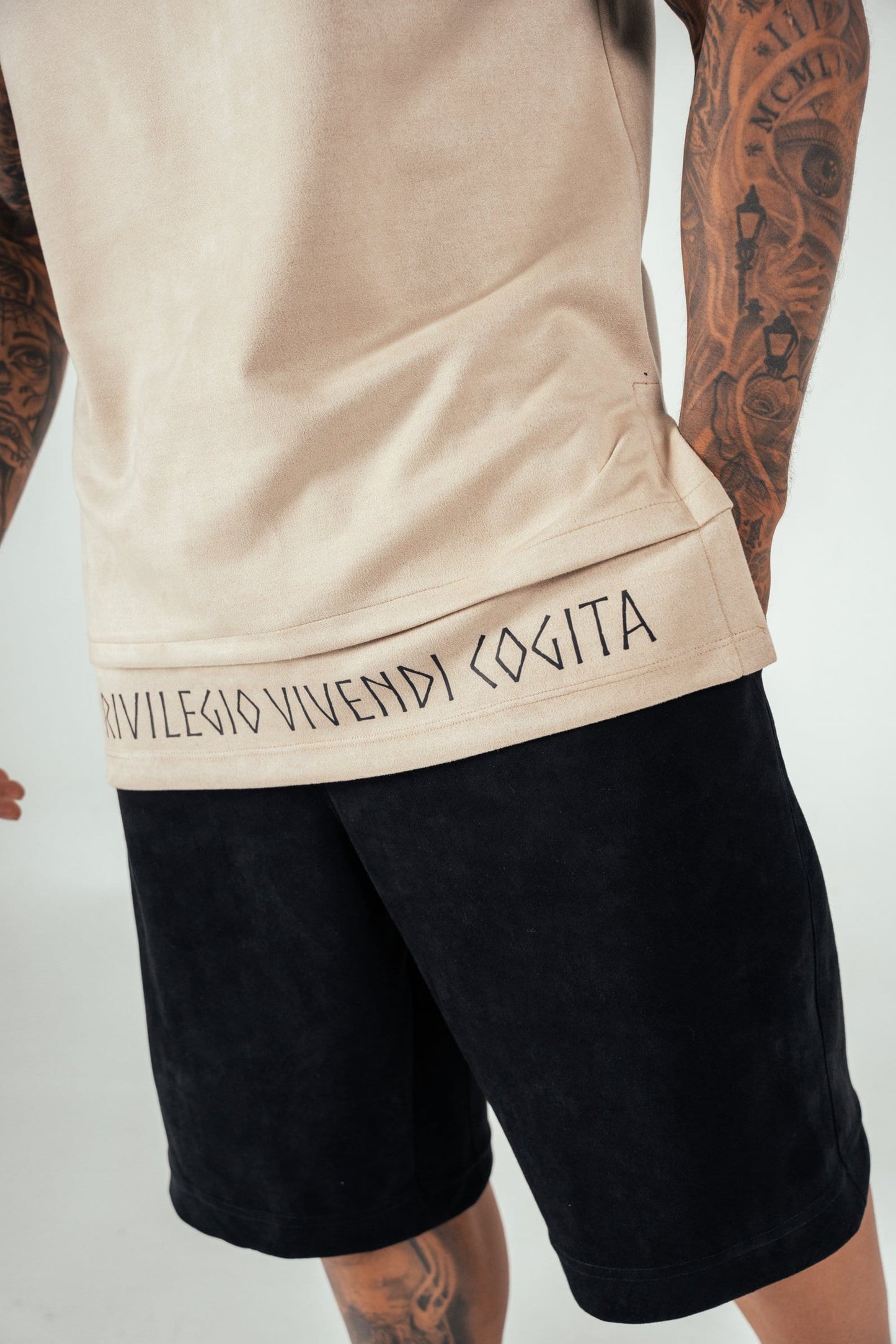 Modern streetwear featuring a beige t-shirt with black lettering and black shorts, highlighting casual fashion and tattooed arms for an edgy, urban look.