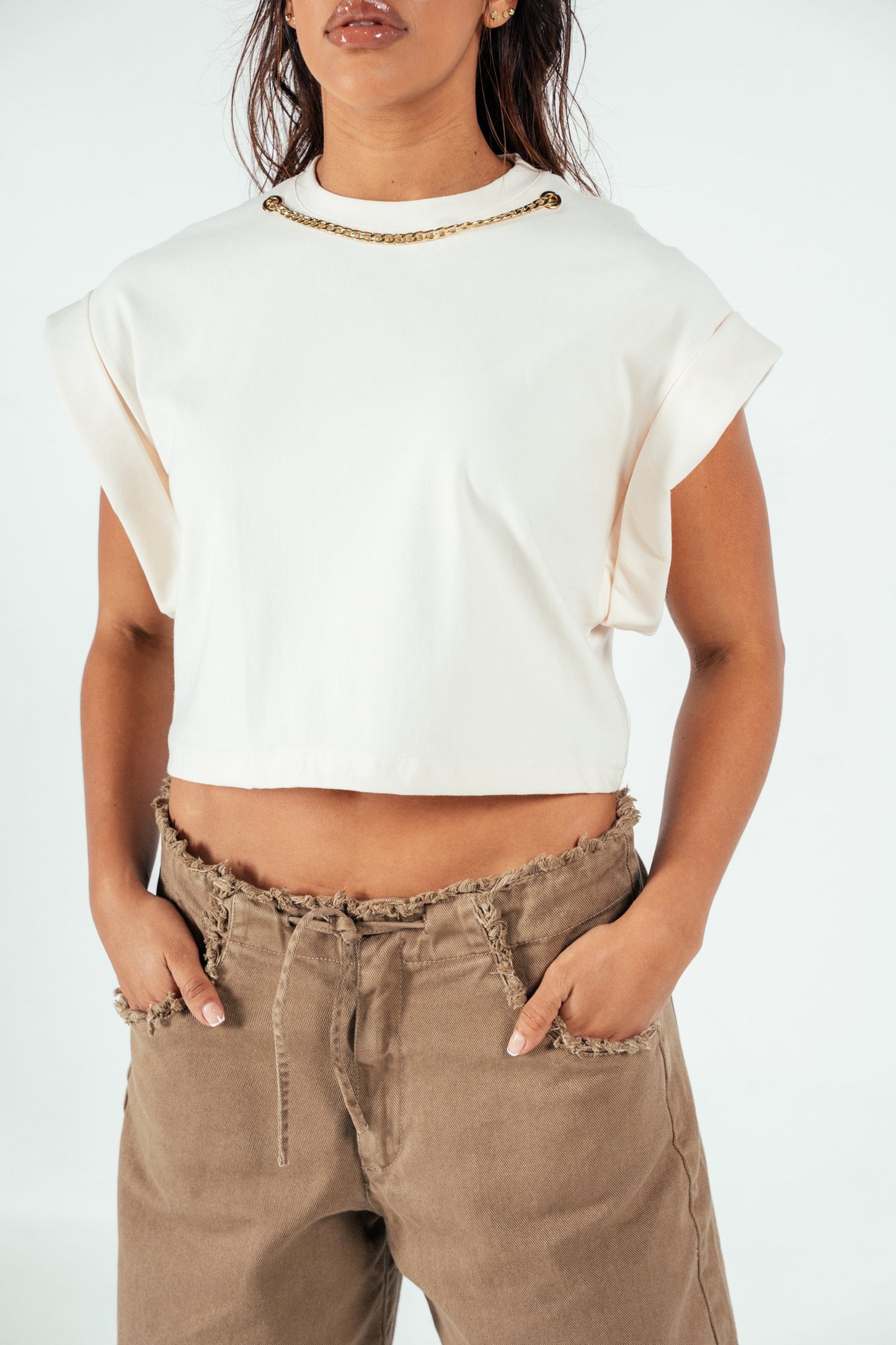 Stylish white crop top with rolled sleeve details, featuring a gold chain embellishment on the neckline, perfect for casual and chic outfits.