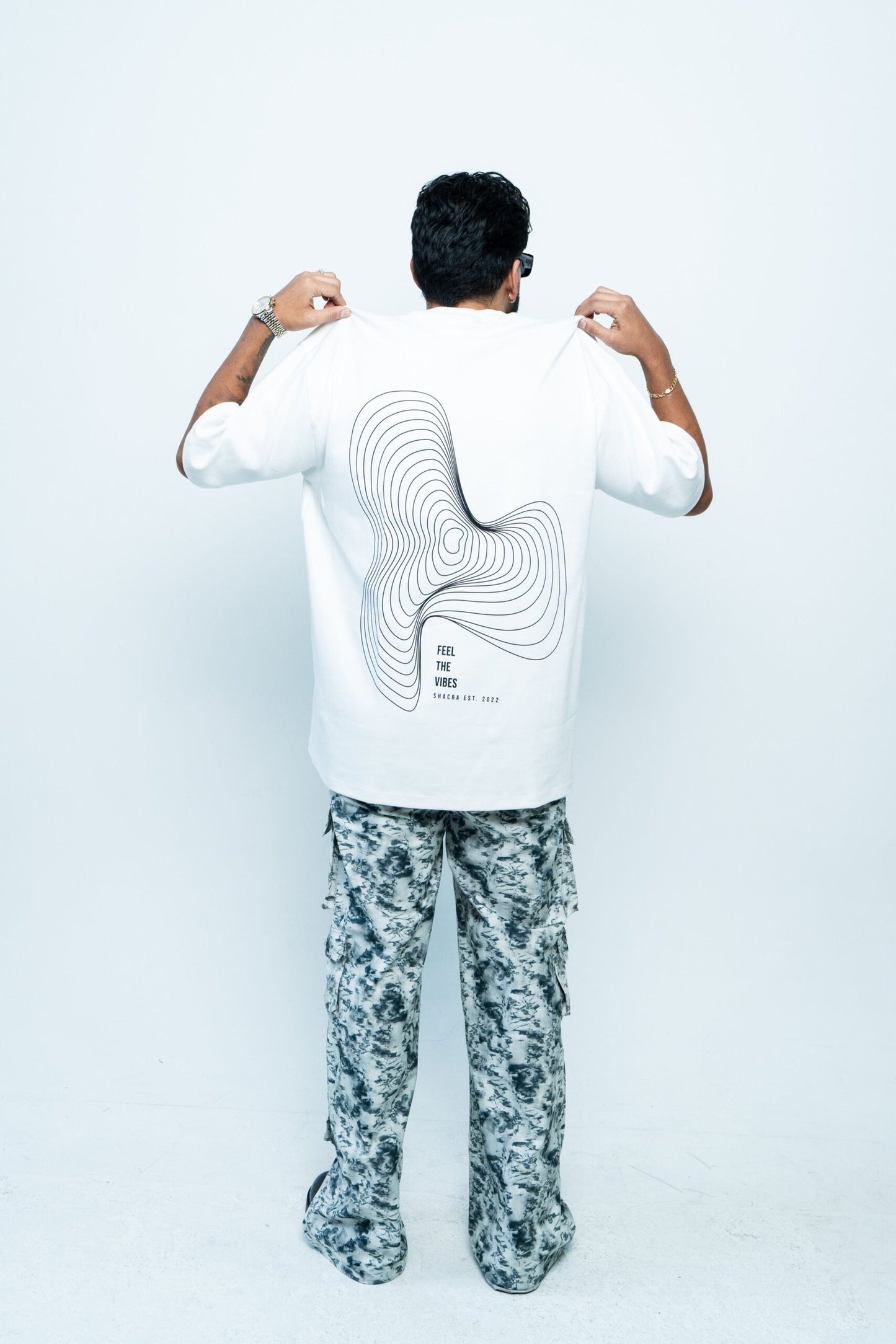 Modern man wearing graphic t-shirt from Shacra brand showcasing contemporary fashion and stylish casual wear, standing against a plain white background, highlighting the apparel design and aesthetic appeal.