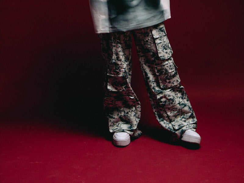 Baggy camouflage cargo pants with white sneakers against a dark red background, streetwear fashion inspiration, trendy urban style, casual menswear, stylish combat trousers.