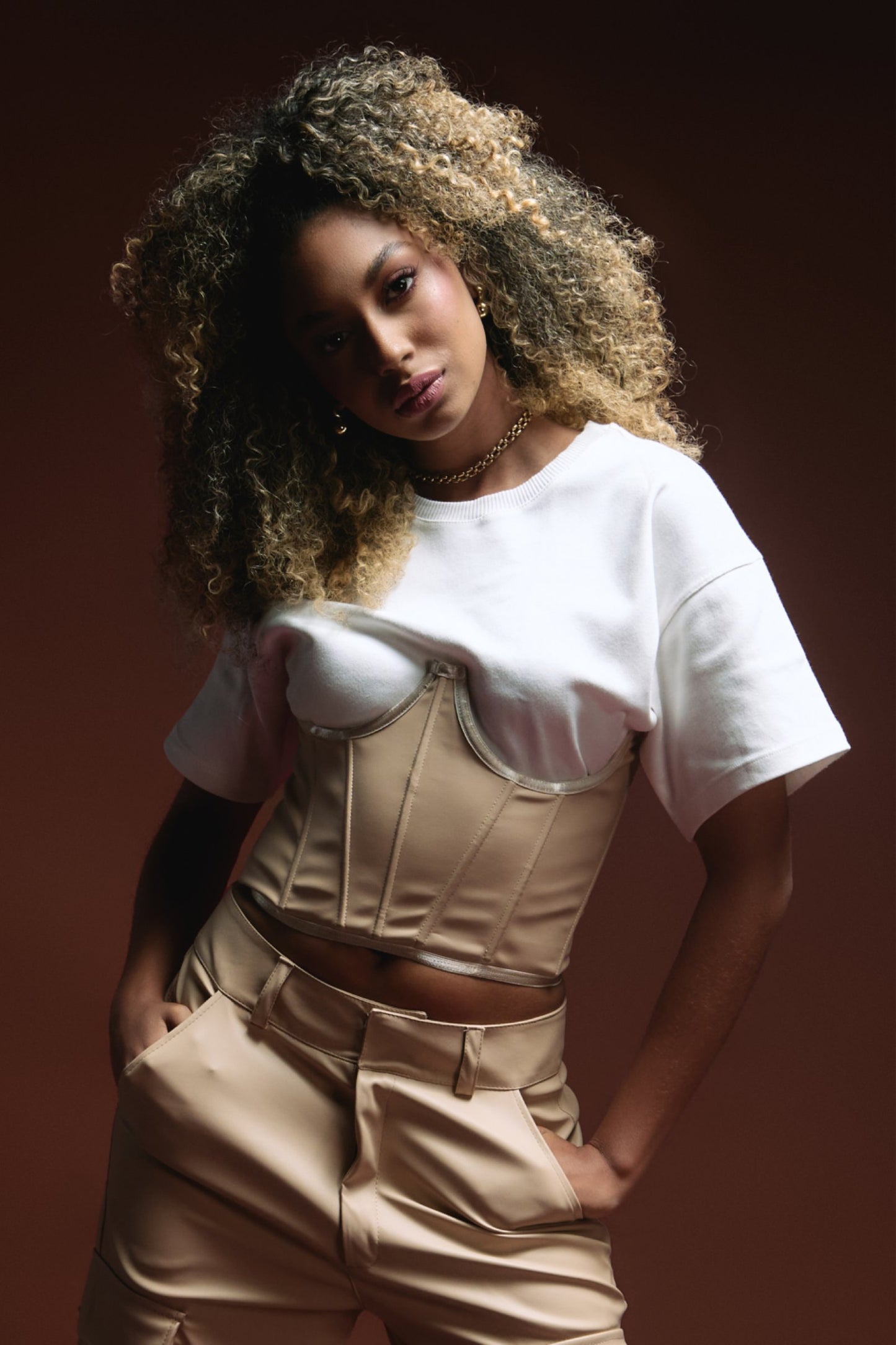 Corset top with beige satin fabric and zipper detail, trendy beige trousers, modern fashion styling, stylish model with curly hair, urban chic outfit, fashion photography for Shacra.