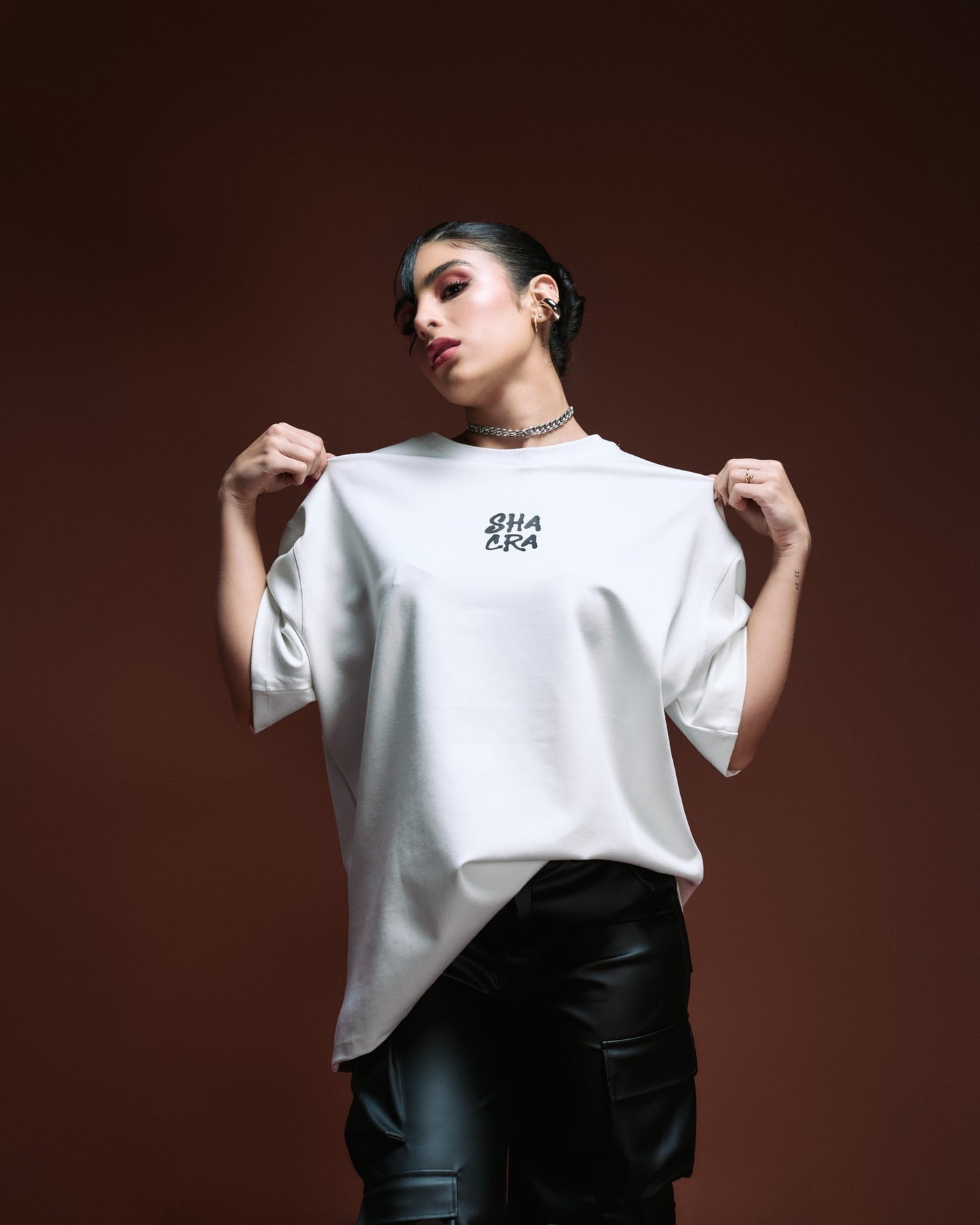 - Casual fashion model wearing a white "SHACRA" t-shirt and black leather pants, showcasing stylish streetwear and modern clothing.
