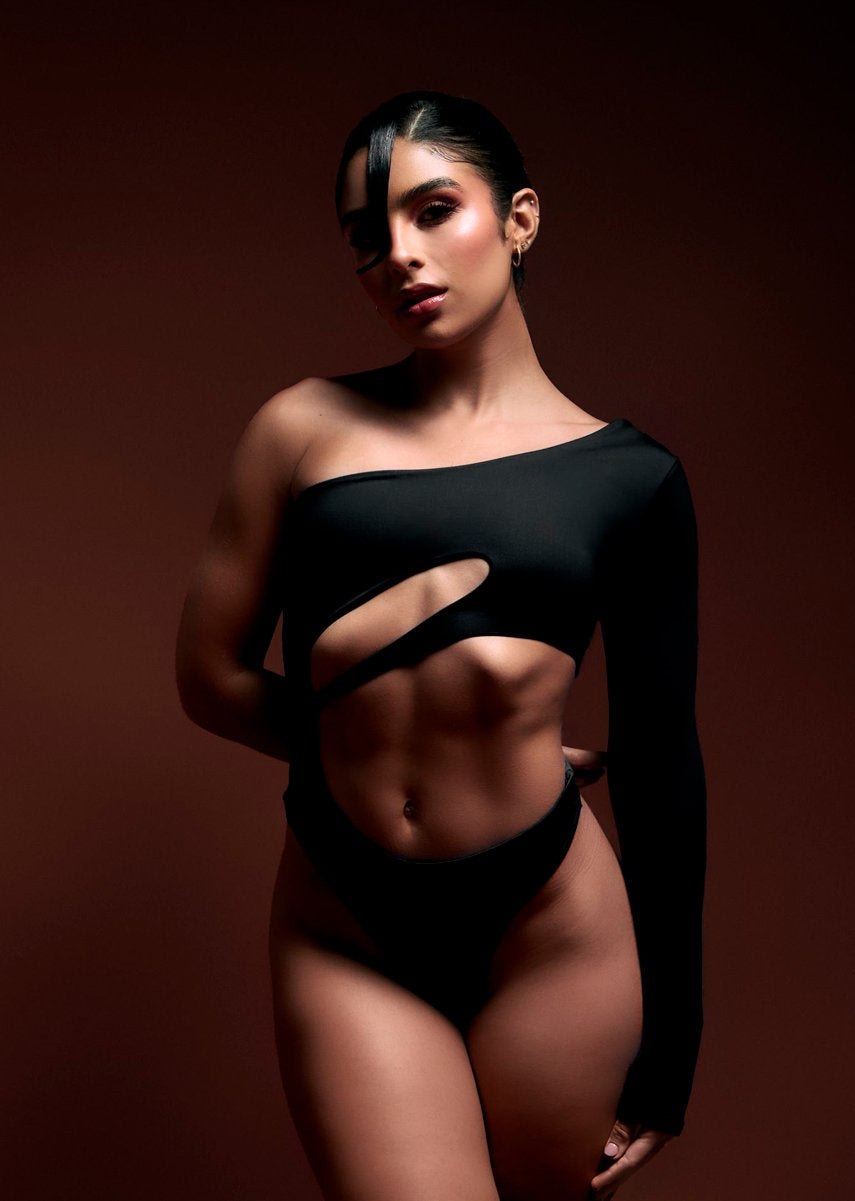 Striking woman with sculpted abs in edgy black cut-out outfit, dark background, high fashion, fitness, empowerment, beauty, body positivity, fashion photography, modern style, confident pose.