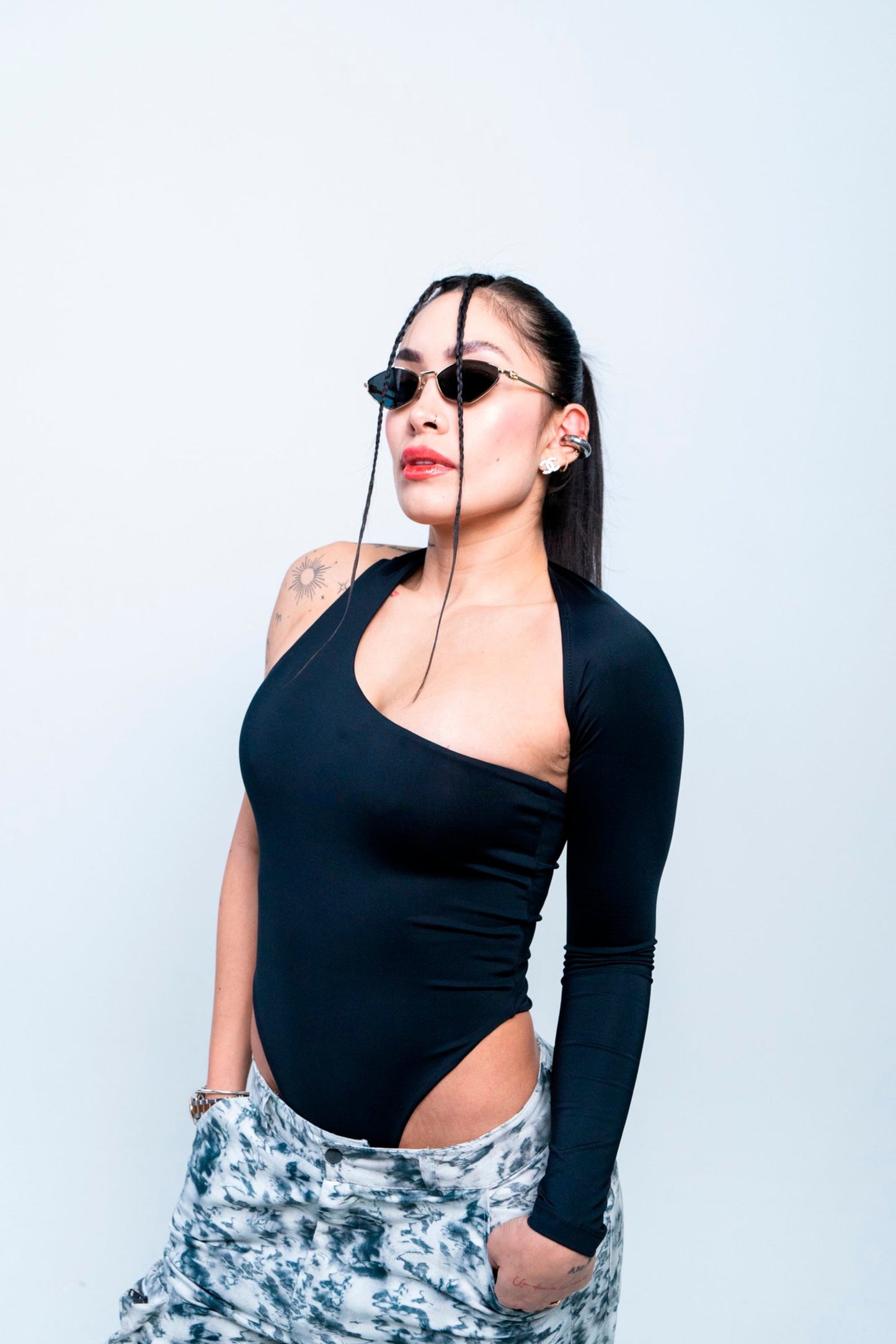 Chic woman wearing stylish sunglasses, black bodysuit, and trendy tie-dye pants, showcasing modern fashion and confident attitude. Perfect for fashion-forward looks and urban style inspiration.