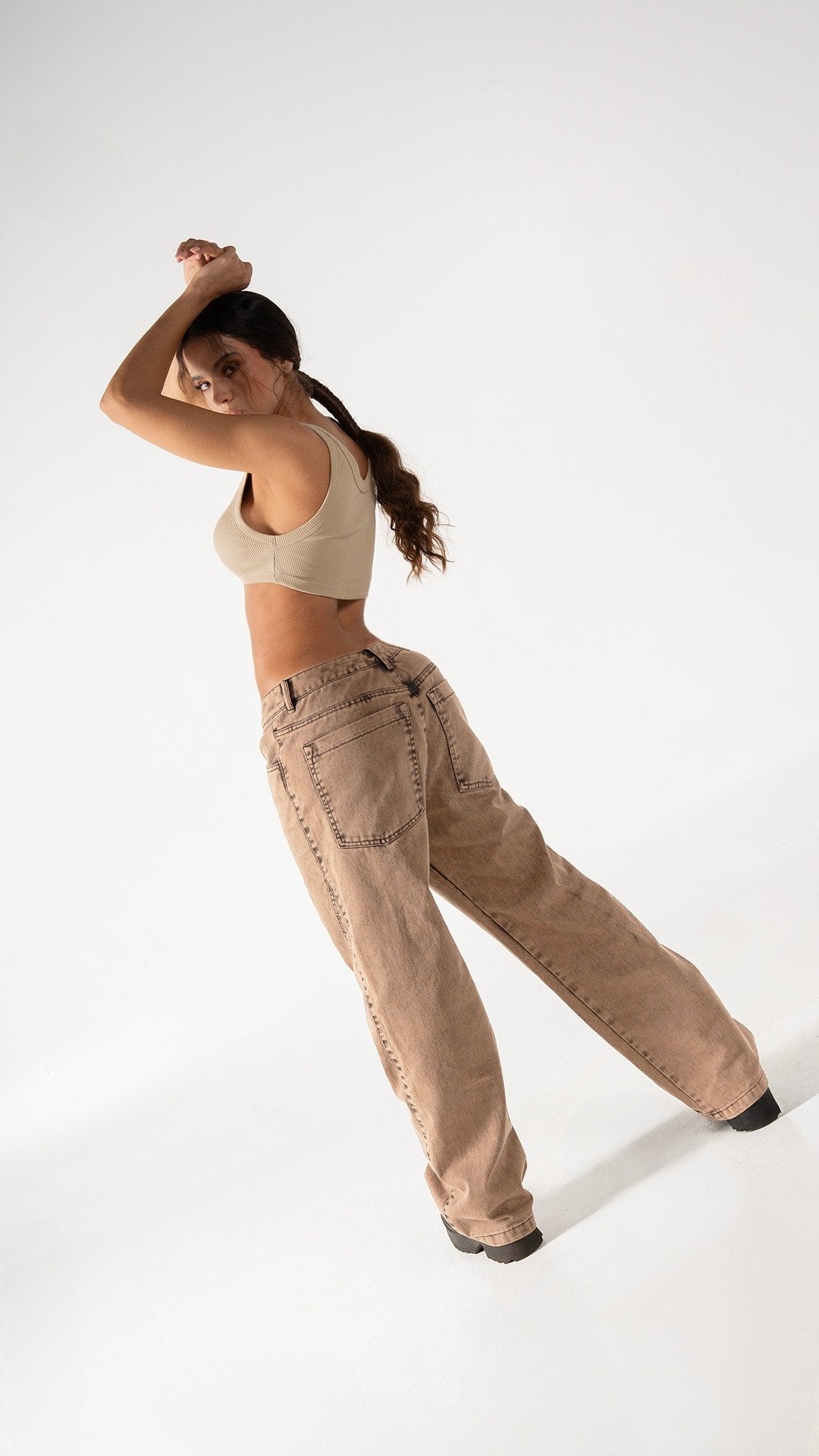 Comfortable casual beige crop top paired with baggy brown jeans, streetwear fashion style, young woman posing confidently in studio setting, modern outfit, trendy look, minimalist background, fashion photography, urban style, autumn fashion, casual chic.