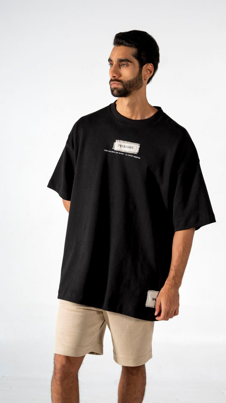 Bold black oversized t-shirt with graphic print, streetwear fashion, casual men's clothing, comfortable everyday wear, paired with beige shorts from Shacra.
