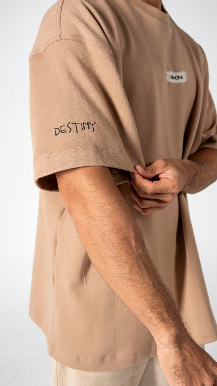 DESTINY tattoo on beige T-shirt, casual streetwear fashion, minimalist clothing, modern style, menswear, comfortable outfit, unique T-shirt design, Shacra fashion brand, trendy street fashion, everyday wear.