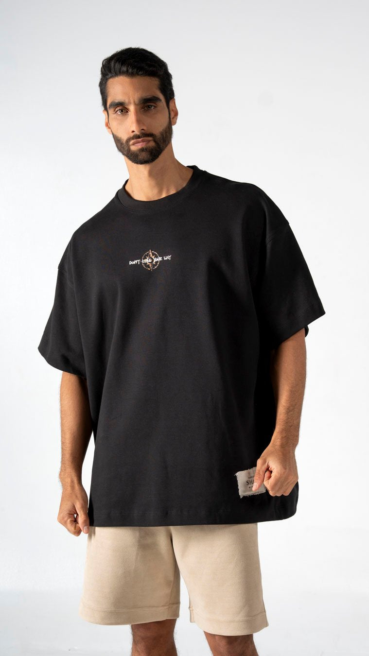 Oversized black graphic t-shirt worn casually by a male model, showcasing contemporary streetwear style, paired with beige shorts, perfect for modern urban fashion looks.