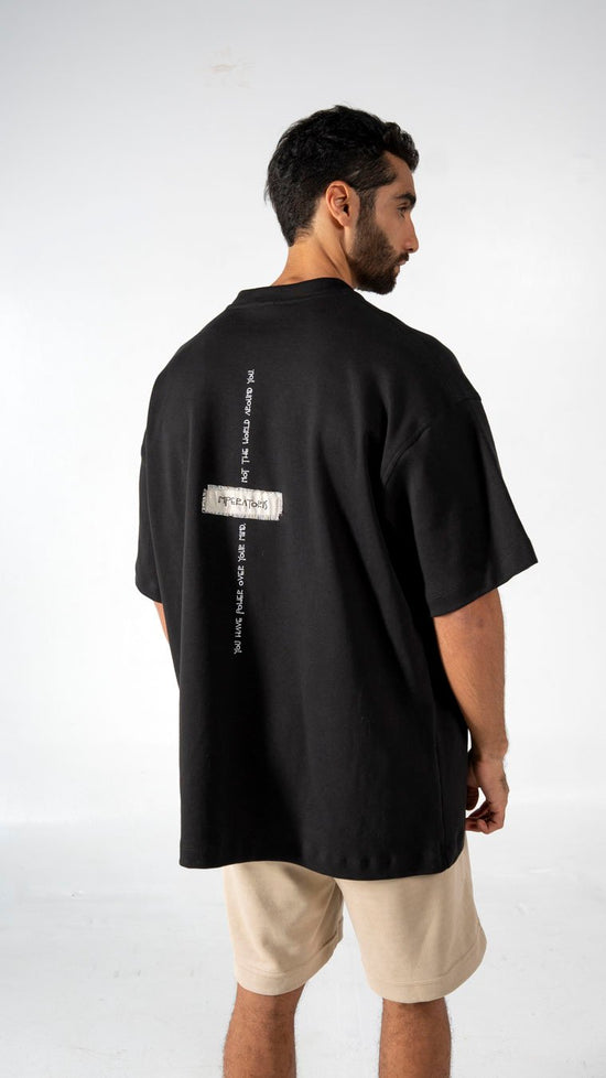 Black oversized graphic t-shirt with layered text design, short sleeves, and modern streetwear style. Perfect for casual fashion looks and urban style outfits.