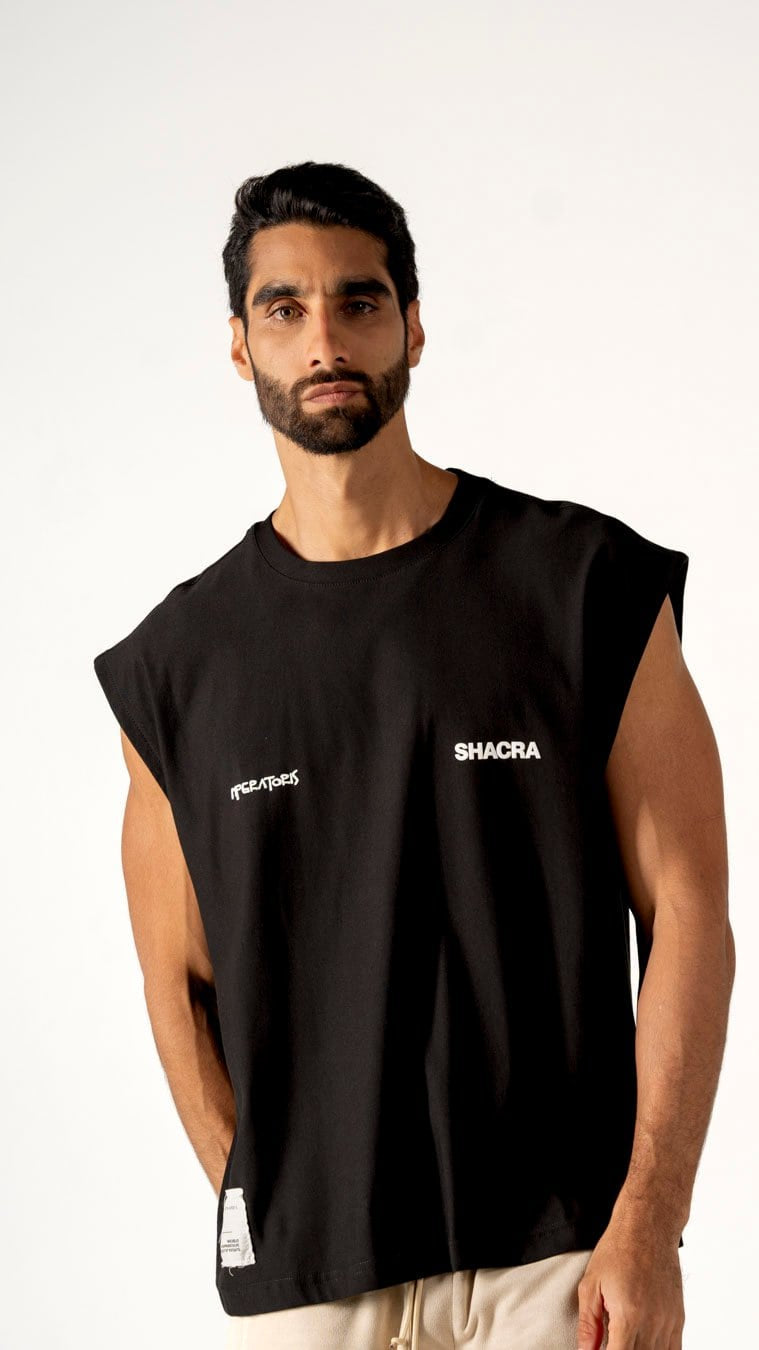 Urban male model wearing black sleeveless T-shirt with "SHACRA" logo for streetwear fashion, against plain white background.