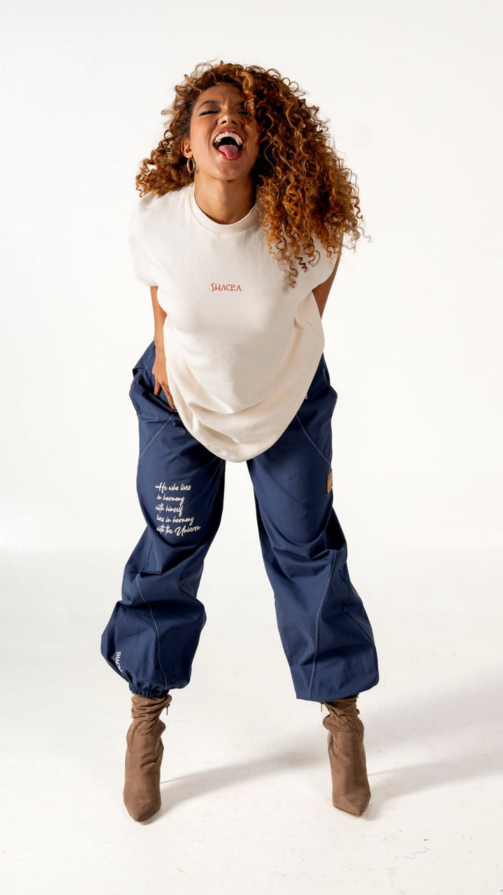 Bright woman with curly hair laughing, wearing casual streetwear and brown boots, posing in studio for fashion brand Shacra, showcasing trendy clothing and confident attitude.