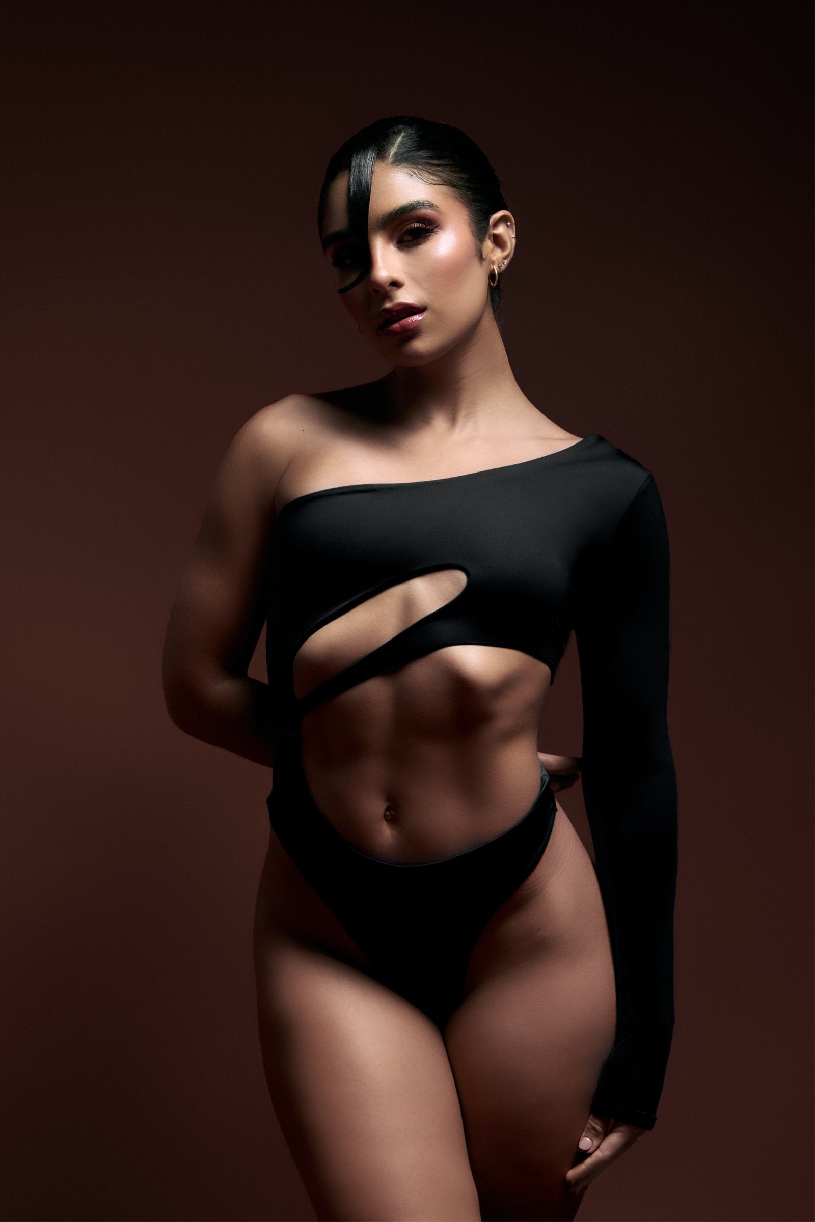 Striking woman wearing a black cut-out fashion top with an asymmetrical design, showcasing modern, high-end fashion and body confidence.