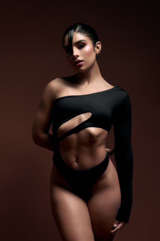 Striking woman wearing a black cut-out fashion top with an asymmetrical design, showcasing modern, high-end fashion and body confidence.