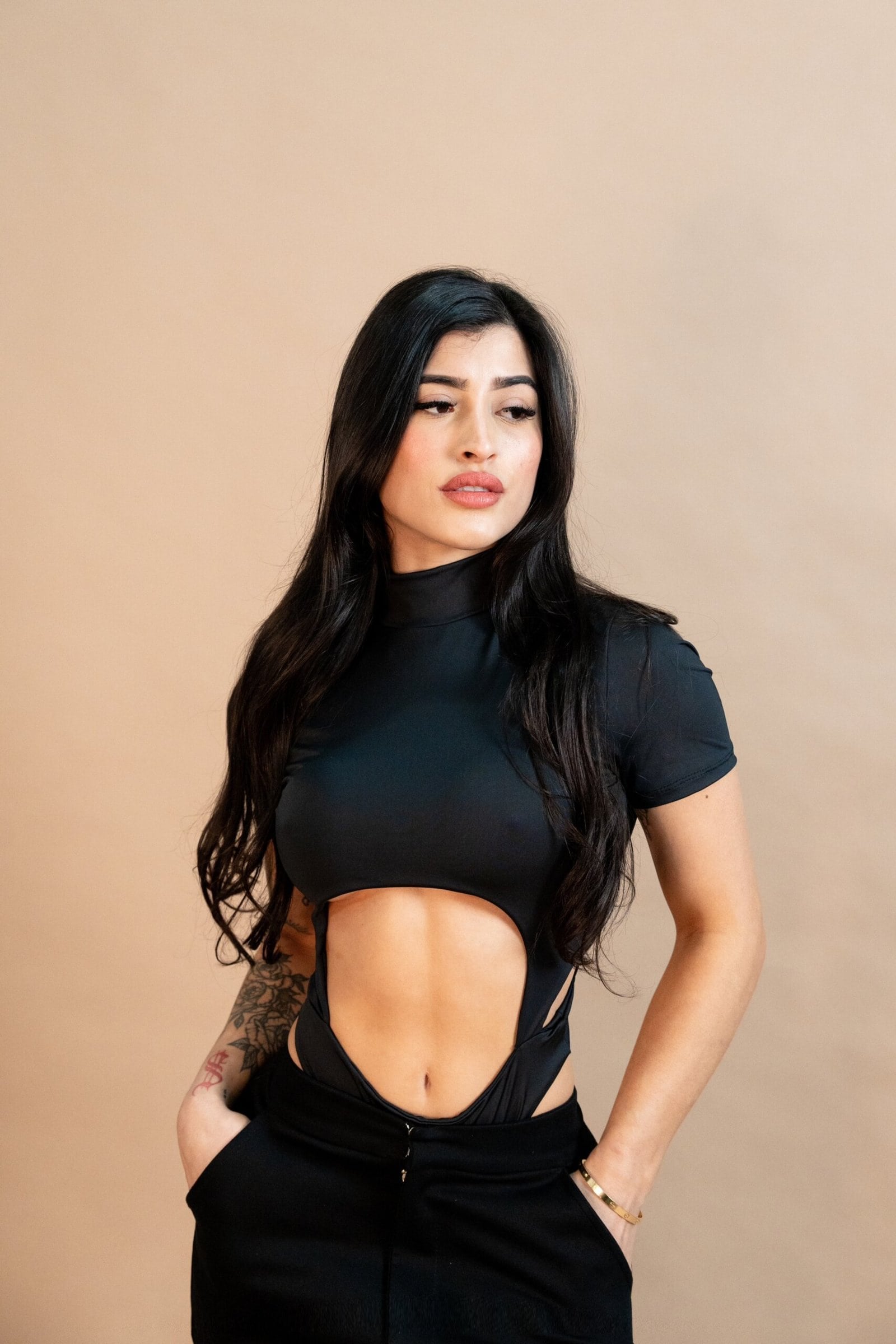 Bold fashion model in a stylish black cut-out top and high-waisted pants, showcasing edgy streetwear and tattoo accessories. Perfect for fashion, street style, and modern casual outfits.
