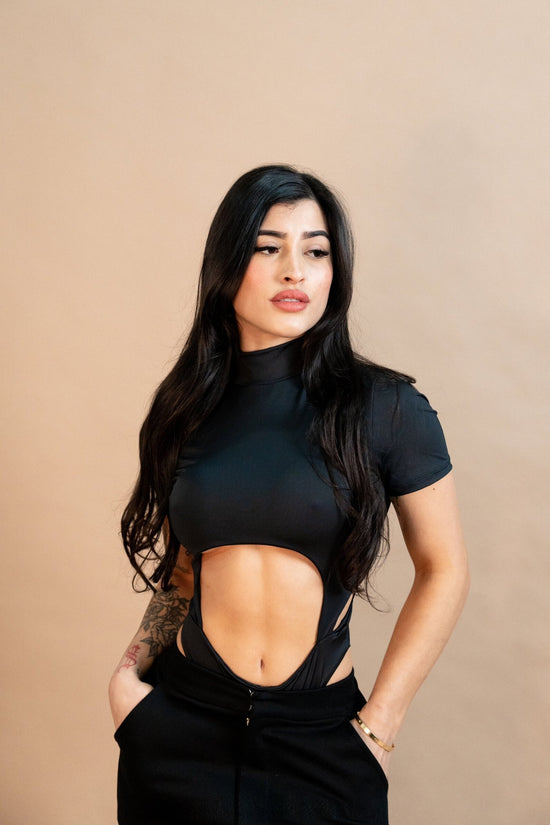 Bold fashion model in a stylish black cut-out top and high-waisted pants, showcasing edgy streetwear and tattoo accessories. Perfect for fashion, street style, and modern casual outfits.