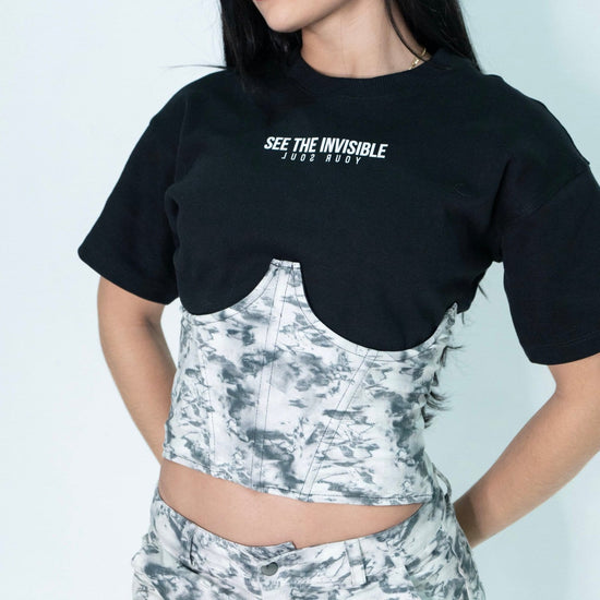 Black graphic t-shirt with "See the Invisible" slogan, layered over a tie-dye bustier, paired with matching tie-dye shorts, embodying a trendy, artistic streetwear look.