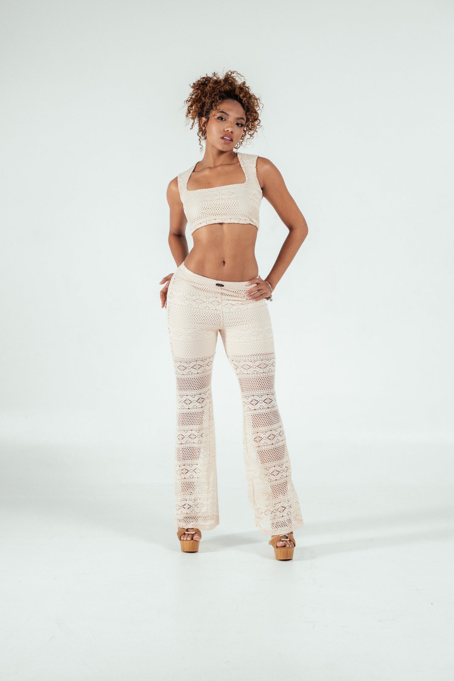Delicate ivory crochet crop top and matching wide-leg crochet pants, stylish bohemian fashion ensemble, perfect for summer or festival outfits, showcased by a confident model on a white background.