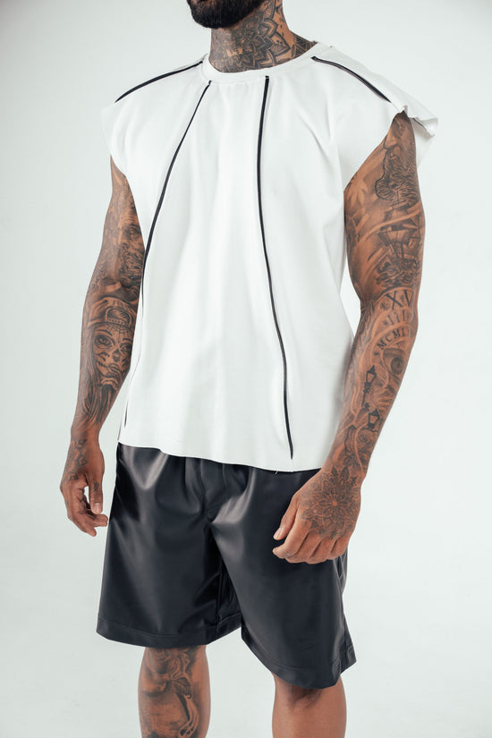 Bold black tattooed arms and neck with a white modern sleeveless shirt featuring black zipper details, paired with black shiny shorts, showcasing contemporary men's fashion and body art.