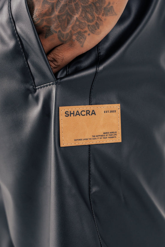 Black leather jacket with a tan label featuring the brand name "Shacra" and a tattooed hand. The image emphasizes fashion, quality craftsmanship, and stylish apparel. Perfect for fashion and accessories SEO.