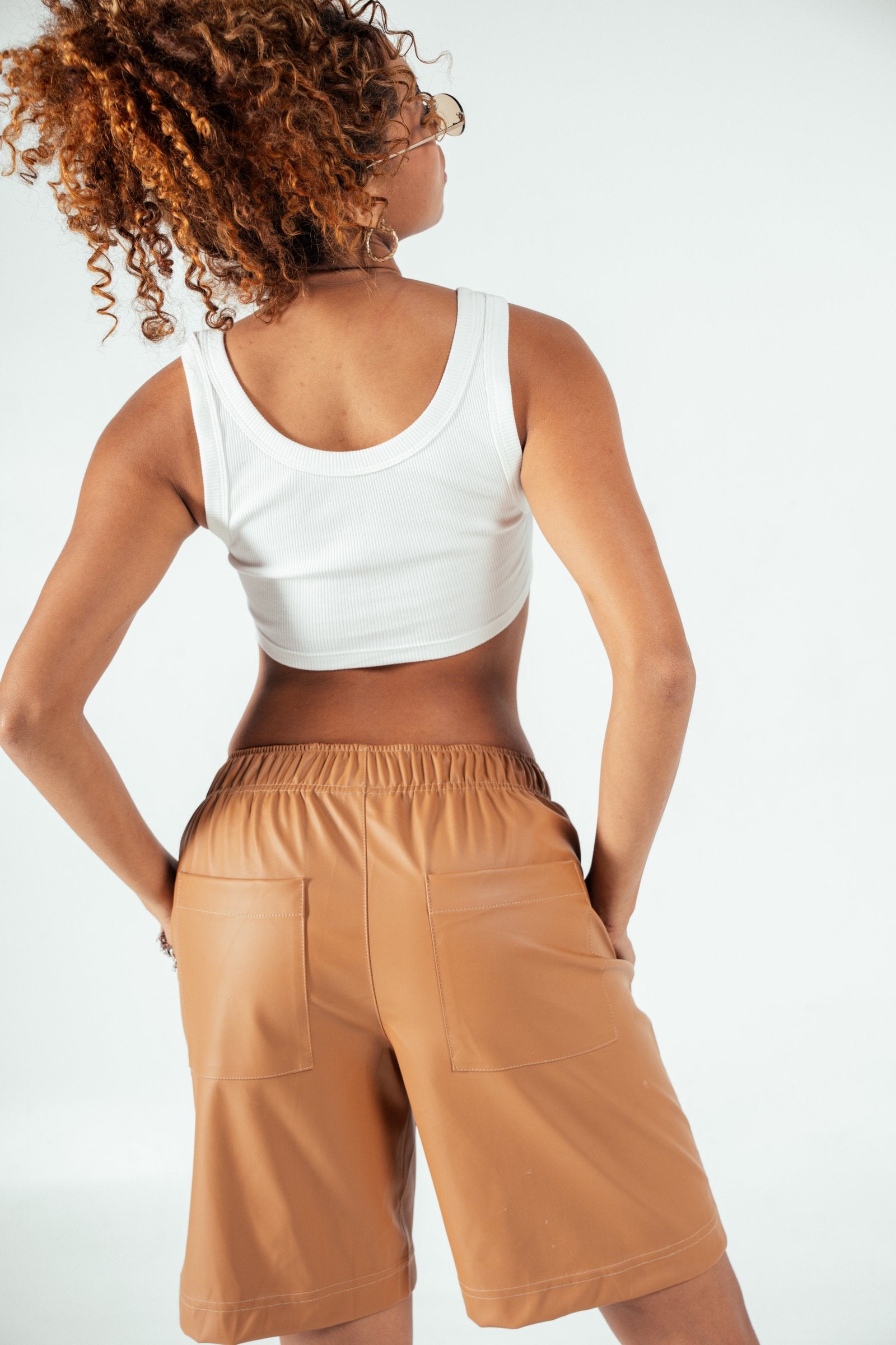 Soft focus on woman with curly hair wearing white tank top and tan shorts, showcasing casual, trendy summer fashion by Shacra. Perfect for inspiring stylish, comfortable everyday outfits.