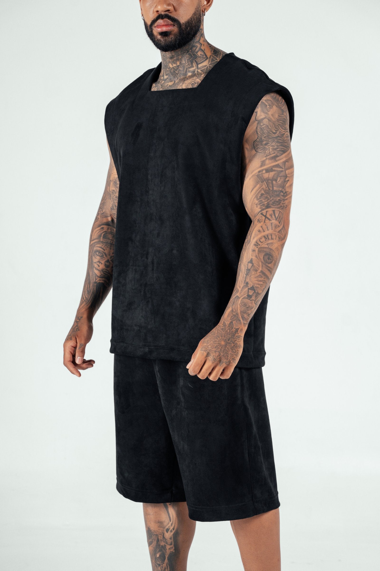 Bold photo of a tattooed male model wearing a black sleeveless top and matching shorts, showcasing contemporary streetwear fashion from Shacra, emphasizing quality and stylish casual clothing.