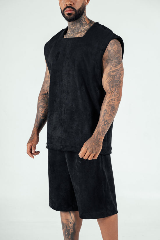 Bold photo of a tattooed male model wearing a black sleeveless top and matching shorts, showcasing contemporary streetwear fashion from Shacra, emphasizing quality and stylish casual clothing.