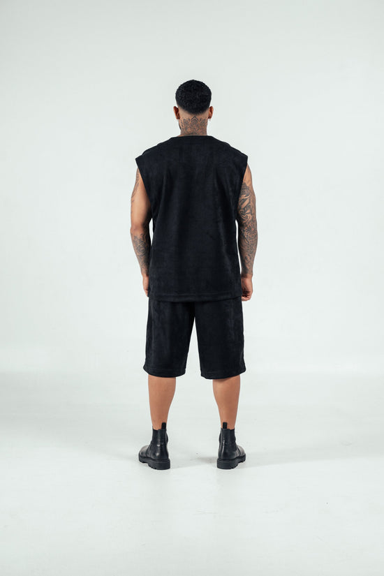 Modern streetwear fashion look featuring a man in all-black outfit with sleeveless top, shorts, and combat boots, showcasing edgy style and tattoos for urban fashion inspiration.