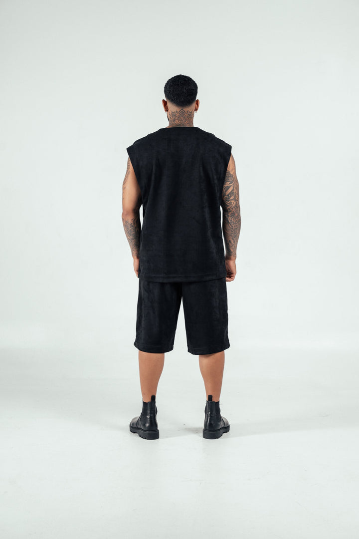 Modern streetwear fashion look featuring a man in all-black outfit with sleeveless top, shorts, and combat boots, showcasing edgy style and tattoos for urban fashion inspiration.