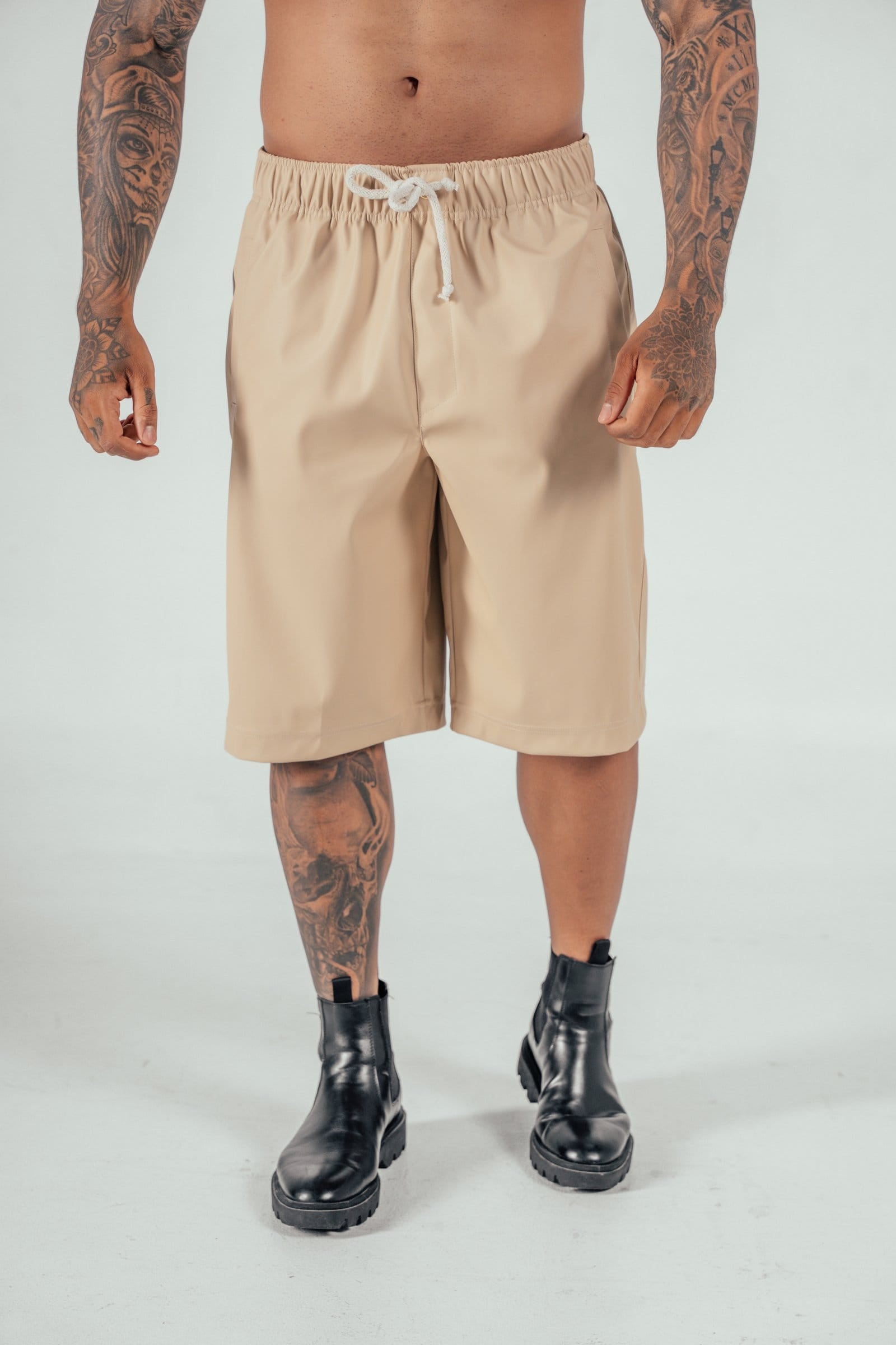 Beige men's casual shorts with drawstring, combat boots, tattooed male model, streetwear fashion, summer clothing, edgy style, men's fashion accessories, stylish streetwear, trendy menswear.