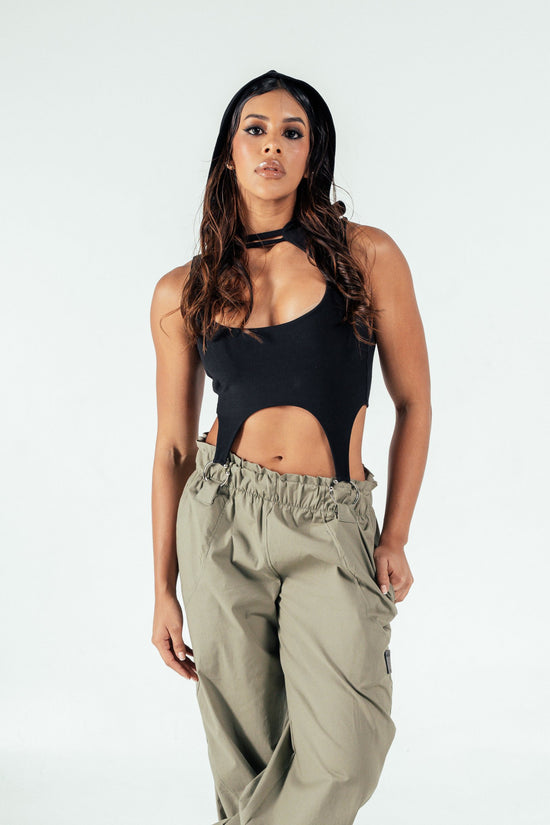 Striking woman with long wavy hair wearing stylish black cutout top and beige cargo pants, showcasing trendy fashion and confident attitude. Perfect for fashion-forward looks and street style inspiration.