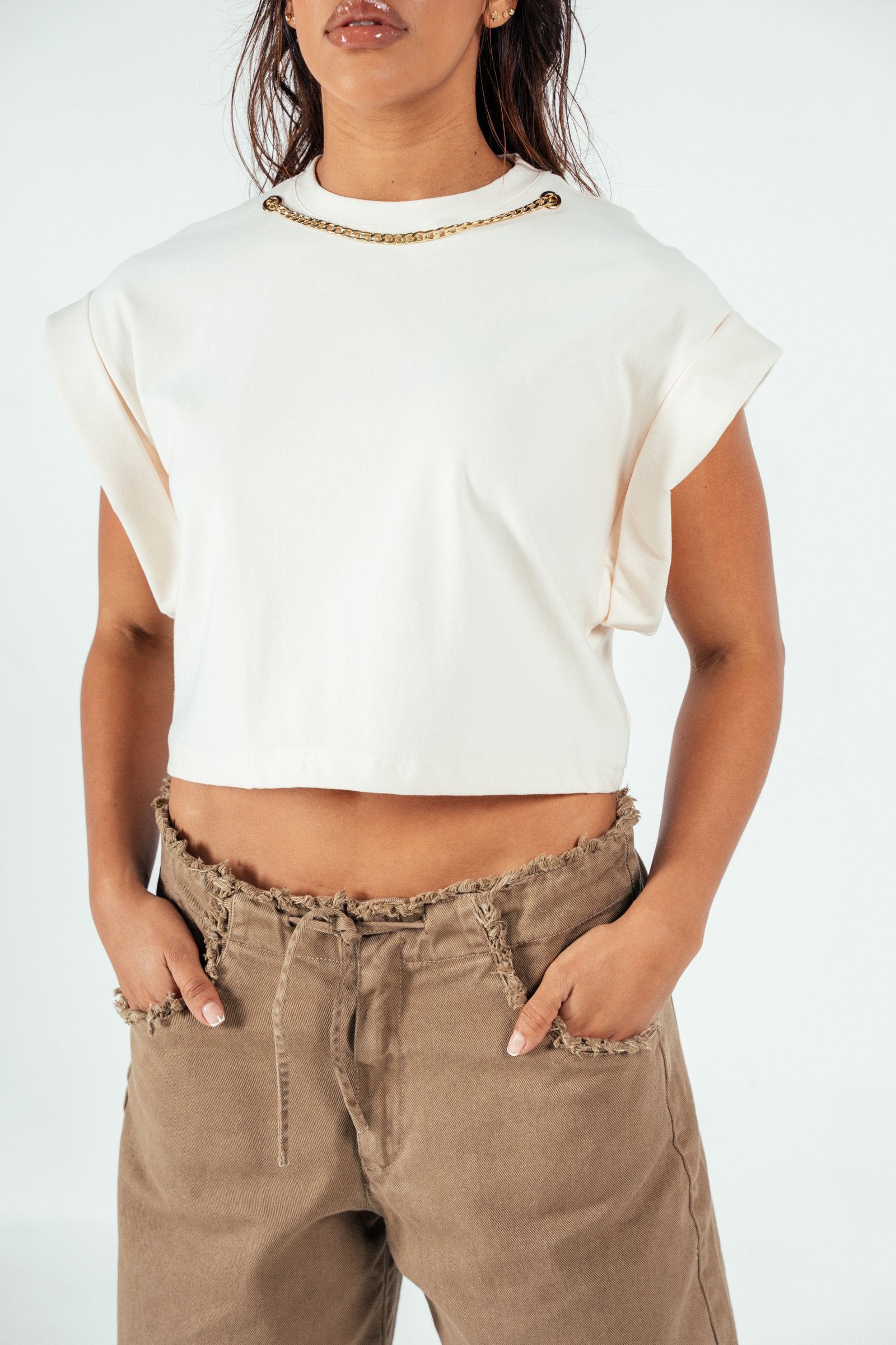 Stylish white crop top with rolled sleeve details, featuring a gold chain embellishment on the neckline, perfect for casual and chic outfits.