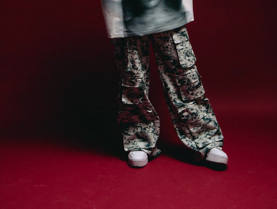 Baggy camouflage cargo pants with white sneakers against a dark red background, streetwear fashion inspiration, trendy urban style, casual menswear, stylish combat trousers.