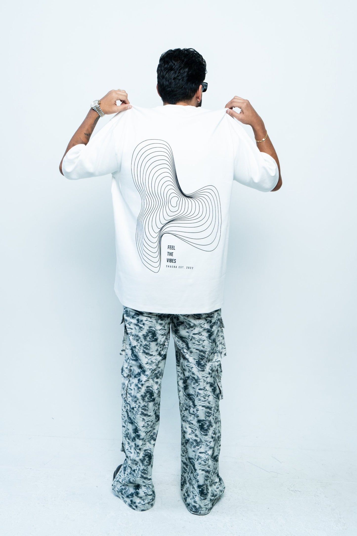 Abstract black and white contour graphic on the back of a man, promoting fashion brand Shacra with the slogan "Feel the Vibes.".