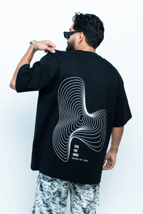 Bold black T-shirt featuring a white contour line abstract design and the phrase "Feel the Vibes" promoting Shacra, a trendy fashion brand established in 2022.