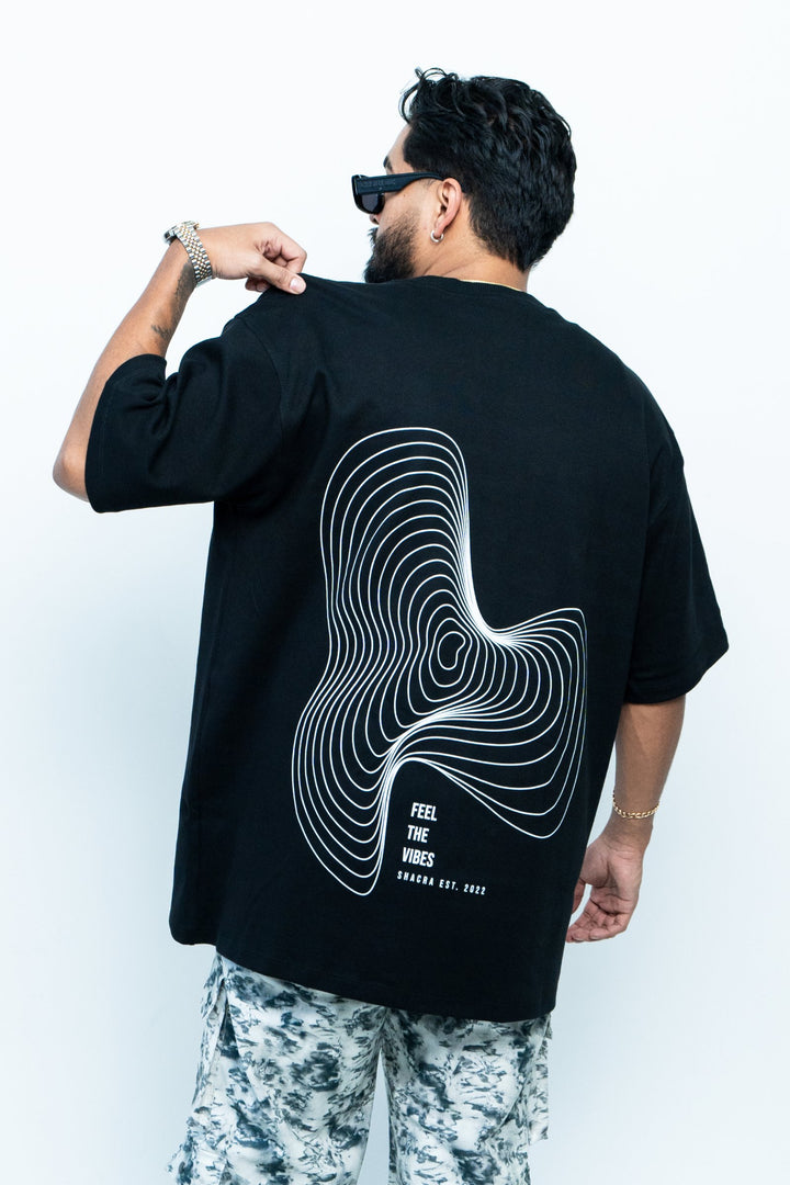 Bold black T-shirt featuring a white contour line abstract design and the phrase "Feel the Vibes" promoting Shacra, a trendy fashion brand established in 2022.