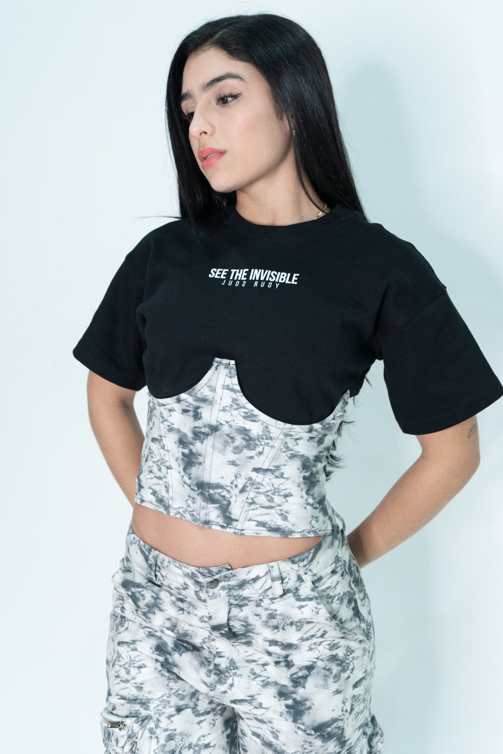 Elegant young woman with dark hair wearing a black t-shirt and marble-patterned crop top, showcasing trendy streetwear fashion and unique clothing styles by Shacra.