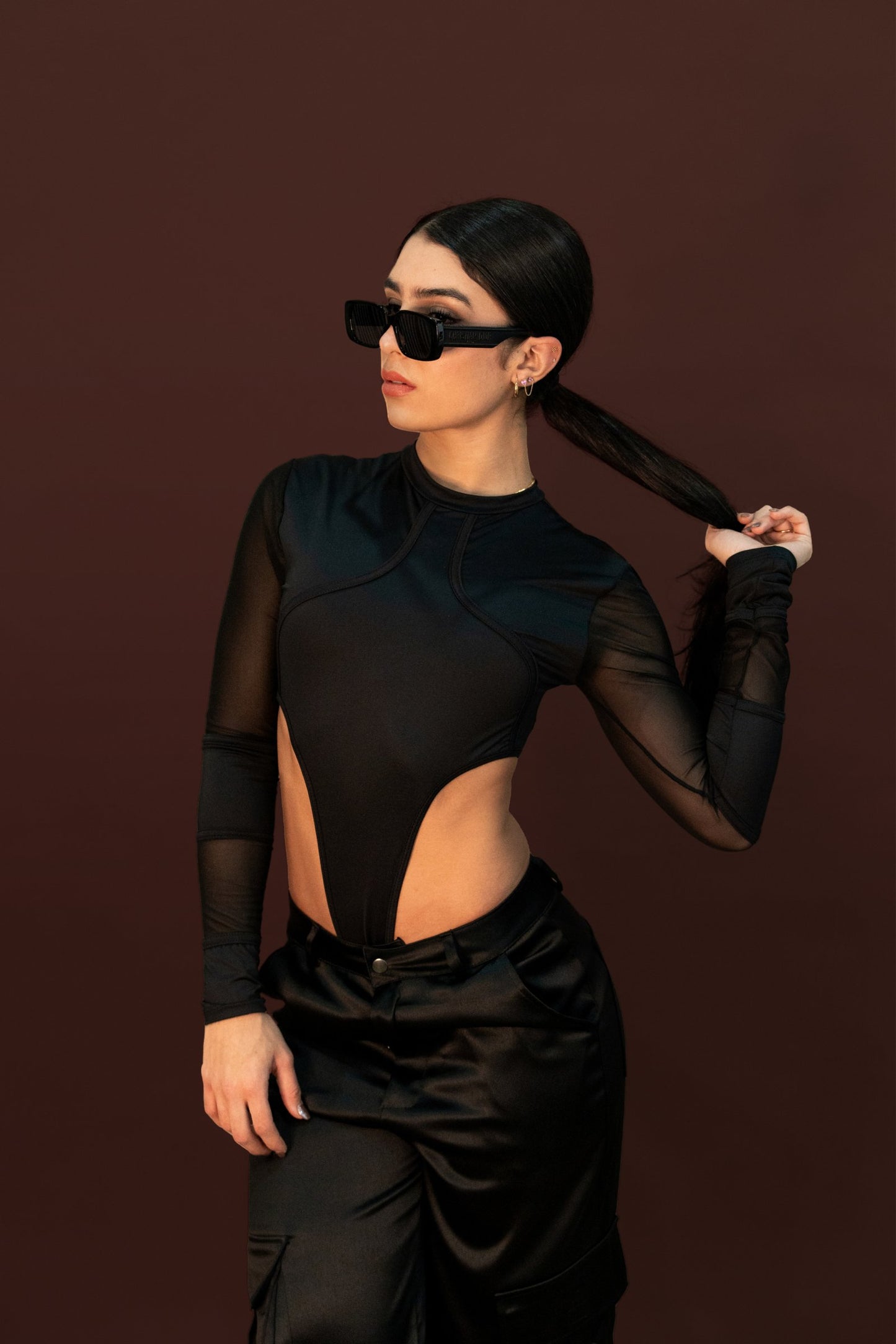Elegant fashion model wearing black mesh bodysuit and oversized sunglasses, showcasing contemporary style and accessories for modern fashion photography.