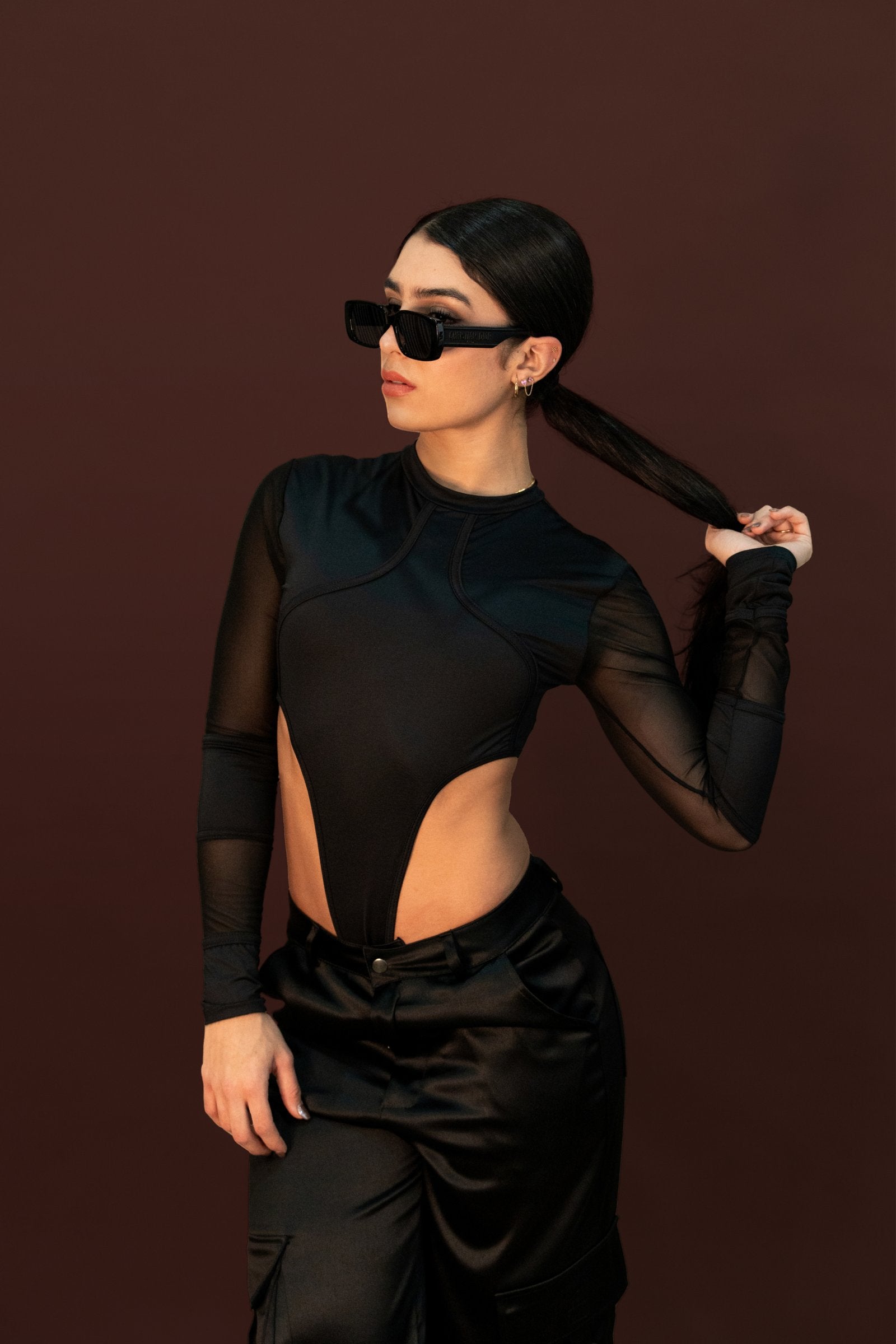 Elegant fashion model wearing black mesh bodysuit and oversized sunglasses, showcasing contemporary style and accessories for modern fashion photography.