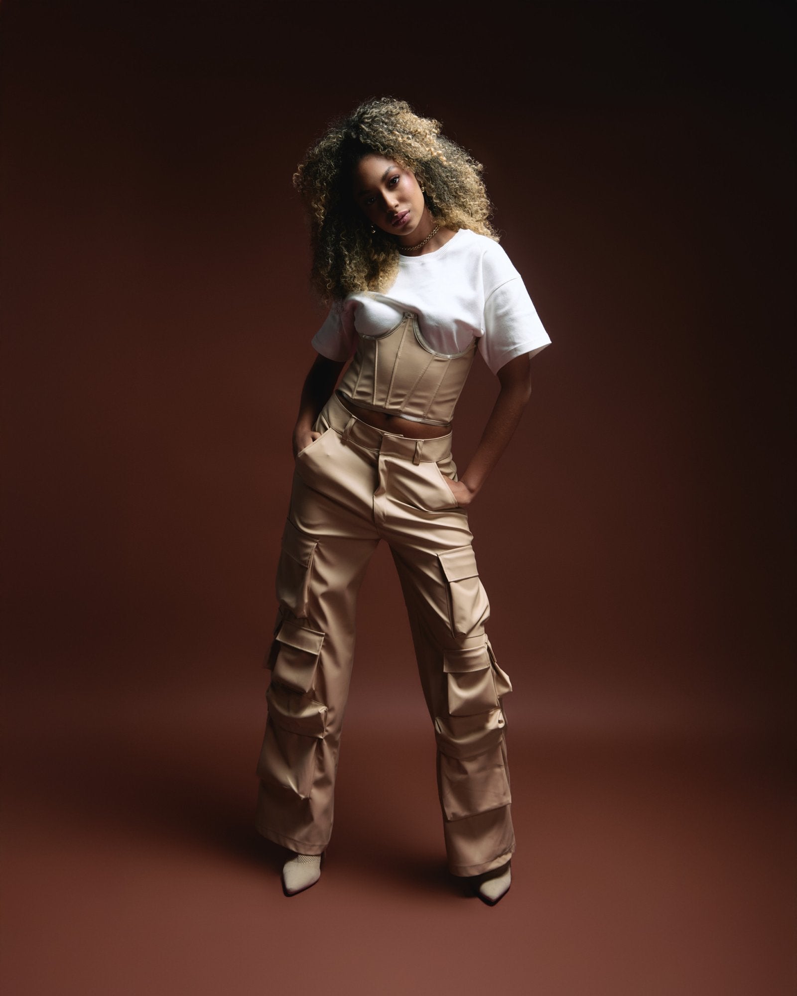 Vegan leather corset over white T-shirt paired with beige cargo pants, styled for a chic, edgy look, shot against a dark studio background for fashion and lifestyle branding.