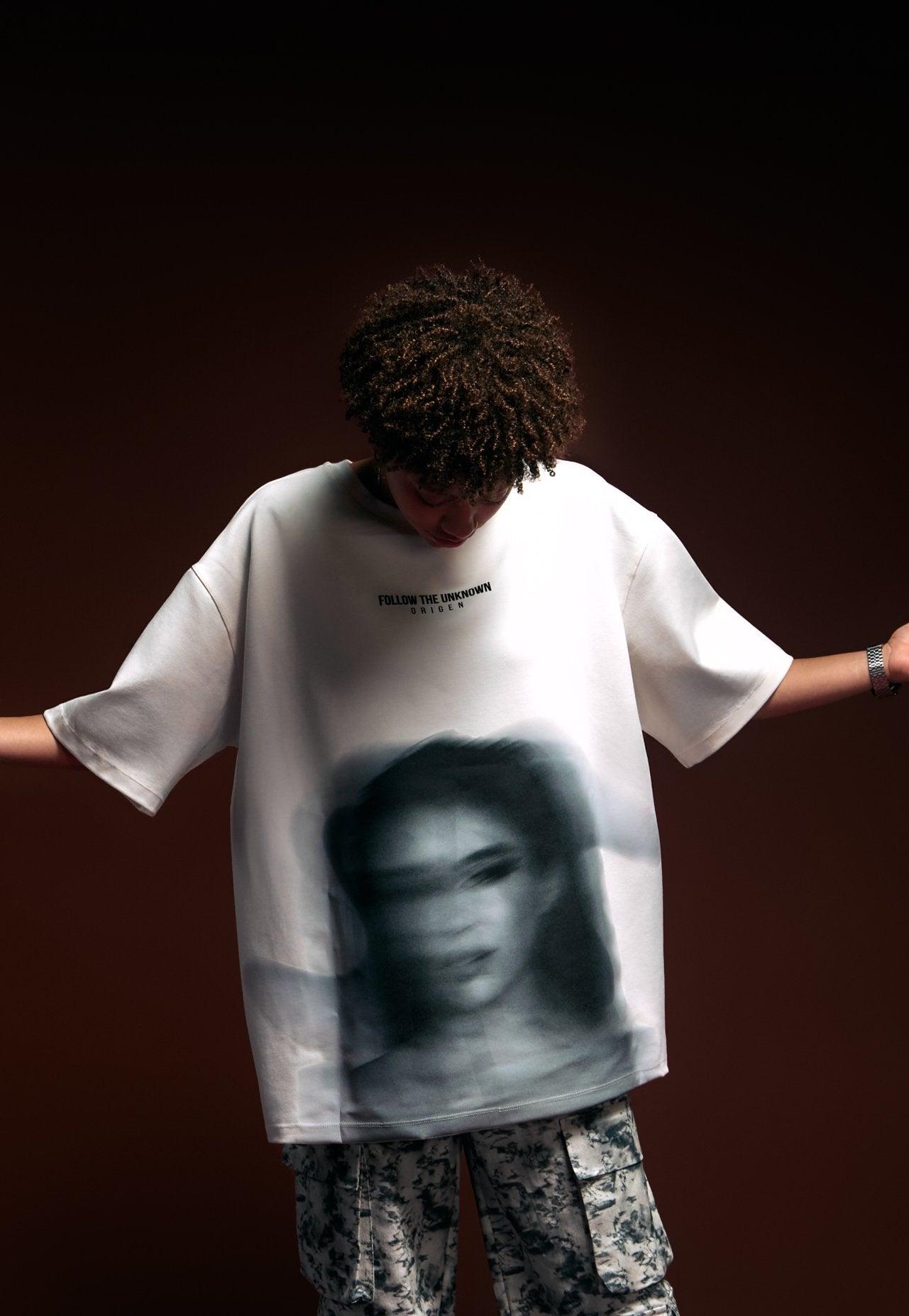 Unique streetwear featuring a printed graphic t-shirt with bold art and the phrase "Follow the Unknown" on a dark background.