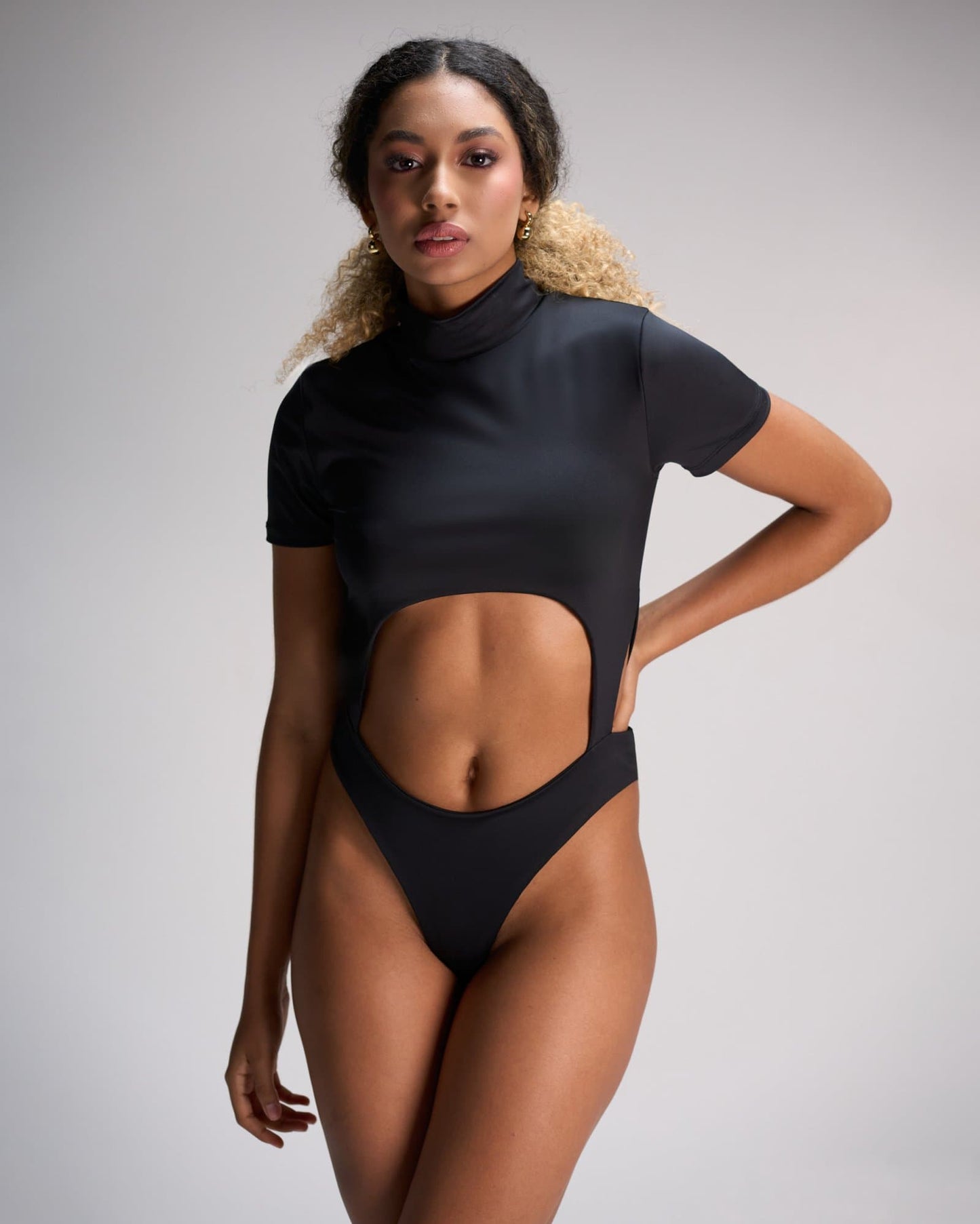 Black cut-out bodysuit fashion, stylish lady posing in studio, modern women's apparel, trendy black outfit, female model, fashion photography, contemporary clothing design, chic and bold wardrobe choice.