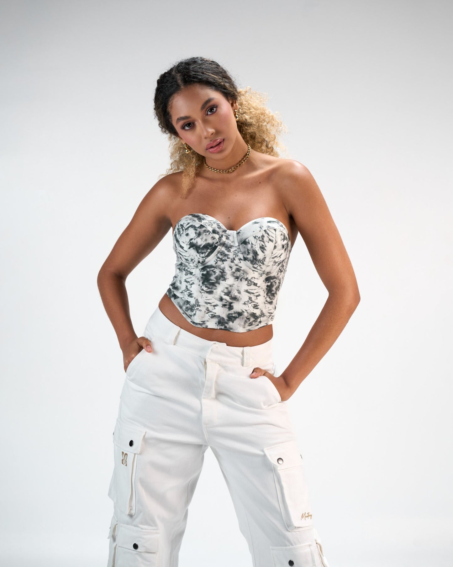 Vibrant young woman wearing a stylish black and white tie-dye bustier top with white cargo pants, showcasing trendy summer fashion in a modern photo shoot for Shacra.